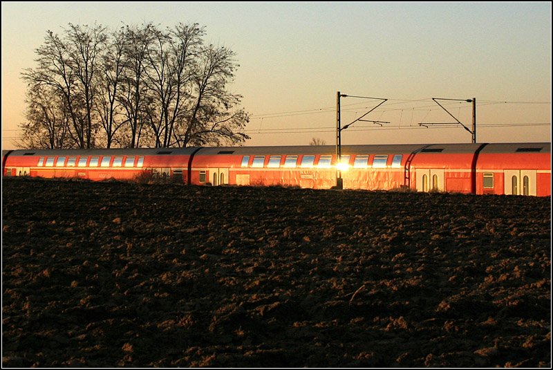 Regionalexpress im letzten Sonnenlicht, Remsbahn. Dunkler Acker vor leuchtend roter Bahn, die etwas im Boden versunken ist. Diese Aufnahme hat es in die Hall of Fame im DSO-Fotoforum geschafft.
