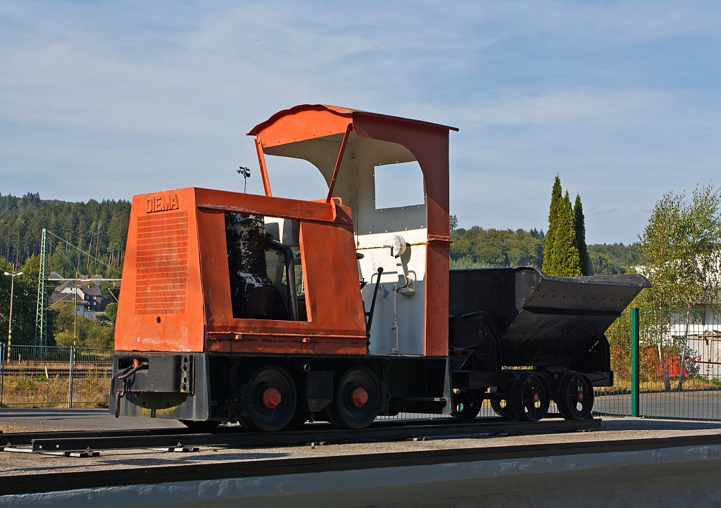 DIEMA-Lok Typ DS12 mit Lore als Denkmallok, am 09.09.2012 in Scheuerfeld (Sieg) vor dem Werktor der Dylus Industrie GmbH (ehem. BAG Feuerfest). Die 600 mm Lok wurde 1949 unter der Fabriknummer 1335 fr Ziegelwerk Chr. Mohring-Shne, Heiningen/Wrtt. gebaut, sie hat eine Leistung von 14 PS bei einem Eigengewicht von 2,8 t. Der Typ DS zeichnet sich aus durch den Antrieb von Motor ber ein Kardangelenk auf ein staubdicht gekapseltes Kegelradachsgetriebe.. Diese Bauart wurde 1934 patentiert.