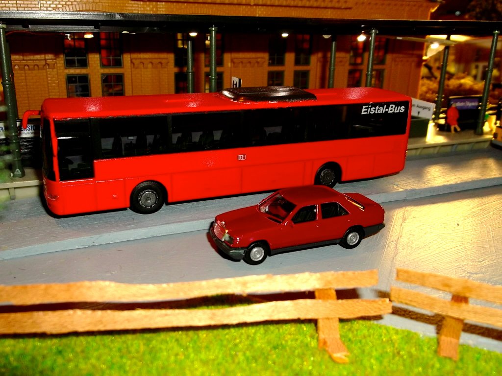 Ein selbst lackierter Mercedes-Benz Integro II (Hersteller AWM) steht am Bahnhof meiner Modelleisenbahnanlage. Der Modellbus wurde von mir in der Original-Farbe  verkehrsrot  (RAL 3020) lackiert und mit dem DB-Logo sowie dem Schriftzug  Eistal-Bus  versehen.  Eistal-Bus  ist die fiktive DB-Regiobus-Tochter meiner Modellwelt.
Im Vordergrund befindet sich ein - ebenfalls selbst lackierter - Mercedes Benz W124 300E.