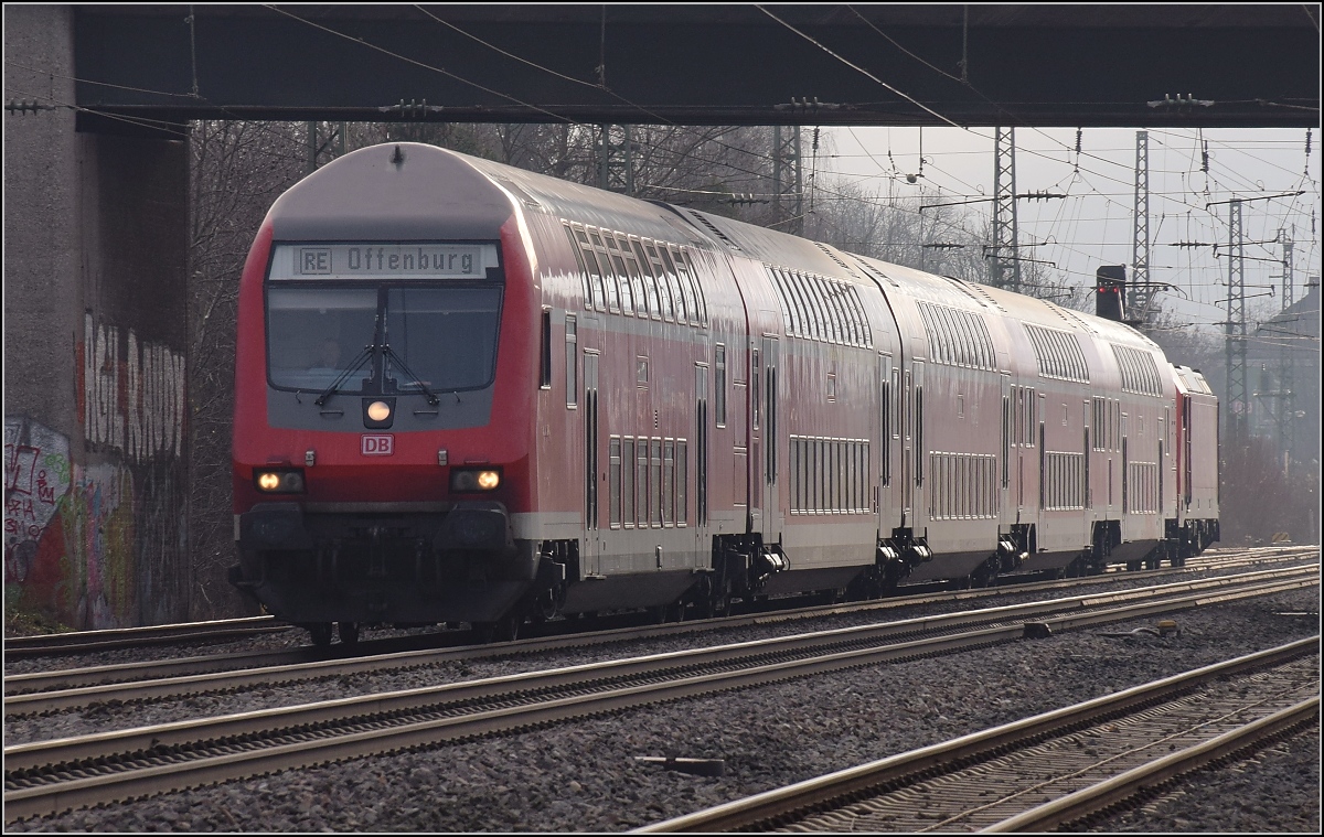 Das Sonnenlicht hat ein Loch im Nebel gefunden und strahlt den RE nach Freiburg von hinten an. Müllheim, Dezember 2018.