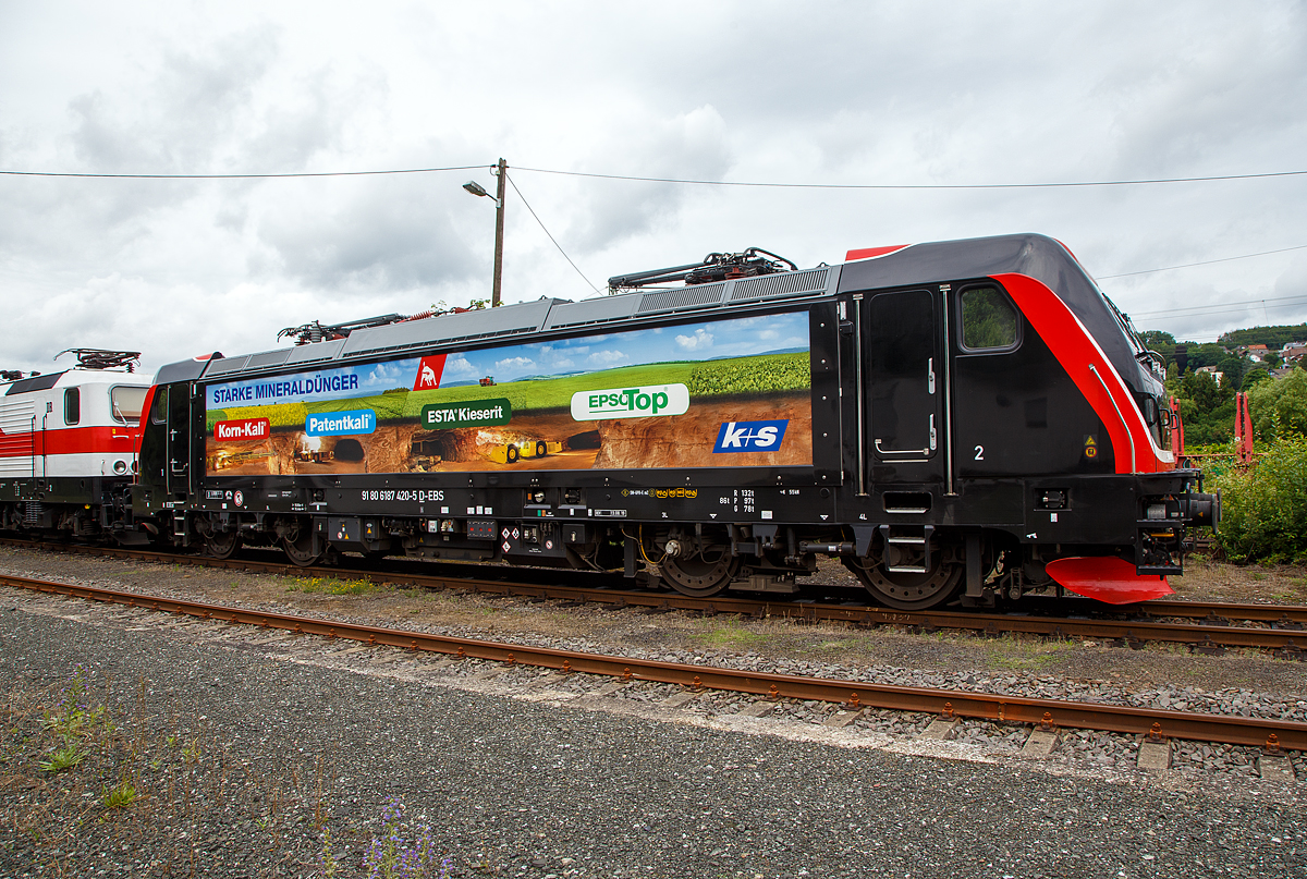 Die Bombardier TRAXX F160 AC3 LM, 187 420-5 (91 80 6187 420-5 D-EBS) der EBS - Erfurter Bahnservice GmbH steht am 05.07.2021 in Scheuerfeld (Sieg) beim Kleinbahnhof der WEBA (Westerwaldbahn), für ihre nächste Aufgabe der Abfuhr von schweren Holzzügen, bereit.

Die Bombardier TRAXX F160 AC3 LMD wurde 2019 von Bombardier in Kassel unter der Fabriknummer 35595 gebaut. Nach meiner Sichtung hat die Lok die Zulassung für Deutschland (D) und Österreich (A). Für Ungarn und Rumänien sind die Zulassungen noch nicht erteilt (H und RO sind durchgestrichen).

Wie die Vorgängerinnen AC1 und AC2 ist die AC3 für den Betrieb unter 15 Kilovolt bei 16,7 Hertz, sowie unter 25 Kilovolt bei 50 Hertz Wechselstrom ausgelegt, und verfügt unverändert über eine Dauerleistung von 5.600 kW und eine Anfahrzugkraft von 300 kN. Von den Traxx 2E übernommen wurde der Maschinenraum mit Seitengang um das sogenannte Powerpack, bestehend aus Stromrichter und Hochspannungsgerüst, womit erstmals alle Varianten dasselbe Layout verwenden.

Neu ist die Kopfform der Traxx-3-Lokomotiven, im Wesentlichen ein auf dem Lokkasten aufgesetztes GFK-Modul. Zudem wurden die Lokomotiven erstmals ab Werk konstruktiv für den Einbau der Zugbeeinflussung ETCS vorbereitet. Neuerungen betreffen die verfügbaren Drehgestelle: zu den bisherigen Varianten „F140“ mit Tatzlagerantrieb und Zulassung für maximal 140 km/h, und „P160“ mit Hohlwellenantrieb und Zulassung für maximal 160 km/h, werden die Traxx-3-Lokomotiven offiziell auch als Variante „F160“ mit Tatzlagerantrieb und Zulassung für maximal 160 km/h angeboten.

Gänzlich neu sind die optional verfügbaren Last-Mile-Module, die es als Last-Mile-Diesel (LMD) mit zusätzlicher Last-Mile-Battery (LMB) gibt. Das LMD besteht aus einem Dieselhilfsmotor und einem Kraftstofftank, um auch nicht-elektrifizierte Streckenabschnitte und Anschlussgleise befahren zu können. Der Dieselmotor von Deutz verfügt über einen Hubraum von 7.150 cm³, erbringt eine Leistung von 230 kW (180 kW am Rad), mit Batterieunterstützung 290 kW und erfüllt die Stage-IIIB-Abgasnorm. Im Dieselbetrieb werden alle vier Fahrmotoren betrieben, die Anfahrzugkraft beträgt dabei mit Batterieunterstützung unverändert 300 kN, ohne Batterie 260 kN. Ohne Anhängelast ist damit eine Höchstgeschwindigkeit von 60 km/h möglich, bei 2000 Tonnen Last noch 40 km/h. Der Tankinhalt von 400 Litern reicht für bis zu acht Stunden Dieselbetrieb, kurze Strecken können auch ausschließlich mit der eingebauten Batterie zurückgelegt werden. Der Übergang vom elektrischen zum Dieselbetrieb kann während der Fahrt erfolgen. Für den Rangierbetrieb ist zudem eine Funkfernsteuerung erhältlich.

Erstmals wurde der Lokkasten nicht mit glatten Seitenwänden gefertigt, sondern konstruktiv deutlich günstiger, sind die Seitenwände der AC3 vertikal gesickt und die Seitenflächen erhielten sogenannte Flex-Panels, eine Vorrichtung zum Einspannen von Planen. Diese würden die Sicken verdecken, und wären kostengünstiger als Umlackierungen oder Umbeklebungen. Die Nutzung der Flex-Panels wurde jedoch in der Schweiz umgehend untersagt.

TECHNISHE DATEN:
Hersteller:  Bombardier Transportation
Spurweite:  1.435 mm (Normalspur)
Achsanordnung: Bo’ Bo’
Länge über Puffer: 18.900 mm
Drehzapfenabstand: 10.440 mm
Achsabstand im Drehgestell: 2.600 mm
Treibraddurchmesser:  1.250 mm (neu) / 1.170 mm (abgenutzt)
Höhe:  4.283 mm
Breite:  2.977 mm
Lichtraumprofil: UIC 505-1
Dienstgewicht:  87 t
Fahrmotoren: 4 Asynchronmotoren
Bremse: Elektrische Bremse (SW-GPR-E mZ)

Daten im Oberleitungsbetrieb:
Höchstgeschwindigkeit: 160 km/h
Dauerleistung: 5.600 kW 
Kurzzeitleistung  Power Boost : 6.000 kW
Anfahrzugkraft: 300 kN
Dauerzugkraft: 252 kN bei 80 km/h
Stromsystem:  15 kV 16,7 Hz~ und 25 kV 50 Hz~

Daten im Dieselbetrieb (Last-Mile):
Nenndrehzahl: 1.800 U/min
Höchstgeschwindigkeit:  60 km/h
Dauerleistung: 230 kW (180 kW am Rad),
Tankinhalt:  400 l