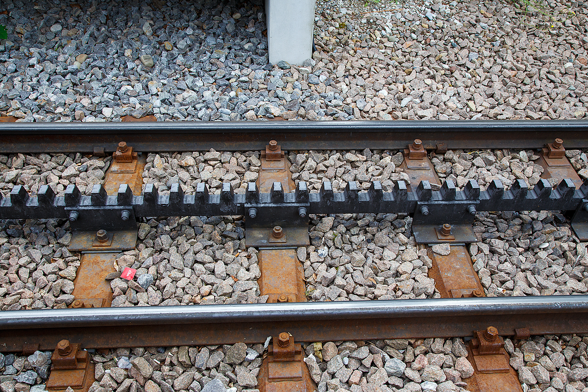 Gleis der Dolderbahn hier am 06.06.2015 an der Bergstation. 

Die Dolderbahn ist eine Privatbahn in der Stadt Zürich. Die Zahnradbahn erschließt (seit 1973, davor Standseilbahn) das Dolder-Gebiet im Quartier Hottingen ab der Haltestelle Römerhof am Römerhofplatz auf 444 Metern über Meer und endet in der Station Dolder auf dem Adlisberg auf 606 Metern über Meer. 

Die Bahn ist in der Spurweite1.000 mm (Meterspur) mit dem Zahnstangensystem von Roll ausgeführt. Die Zahnstangen sind hochliegend (über der Schienenoberkante).
 
System Von Roll:
Die von der Firma Von Roll (heute Tensol) entwickelte Zahnstange ist nur dem Namen nach eine Lamellenzahnstange, nämlich eine einlamellige. Sie hat dieselbe Zahnteilung (100 mm) wie die Riggenbach'sche und die Strub'sche Zahnstange. Von letzterer unterscheidet sie sich in der Grundform: einfaches Breitflach-Profil anstatt einer Keilkopfschiene ähnliches Profil. Die Von Roll Zahnstange kommt in erster Linie bei Neubauten sowie als preisgünstiger Ersatz alter Zahnstangen nach den Systemen Riggenbach oder Strub zur Anwendung. Sie ist zwar dicker (30–80 mm, je nach Zahndruck) als eine der Lamellen nach Abt, doch ihre Biegsamkeit ist ausreichend, um flexibler als die Originale nach Riggenbach oder Strub anwendbar zu sein. Sie kann auch durchgehend verschweißt werden. Zur Befestigung auf den Schwellen dienen besondere Profilstahl-Sättel.

Die Systeme Von Roll, Riggenbach und Strub können miteinander kombiniert werden, d.h. in einer Zahnradbahn können Zahnstangen nach allen drei Systemen verbaut sein. Wobei man heute eigentlich aus Kostengründen nur noch Von Roll-Zahnstangen verbaut, da diese Lamellenzahnstangen auf einer automatischen Spezialmaschine präzis und wirtschaftlich hergestellt werden.