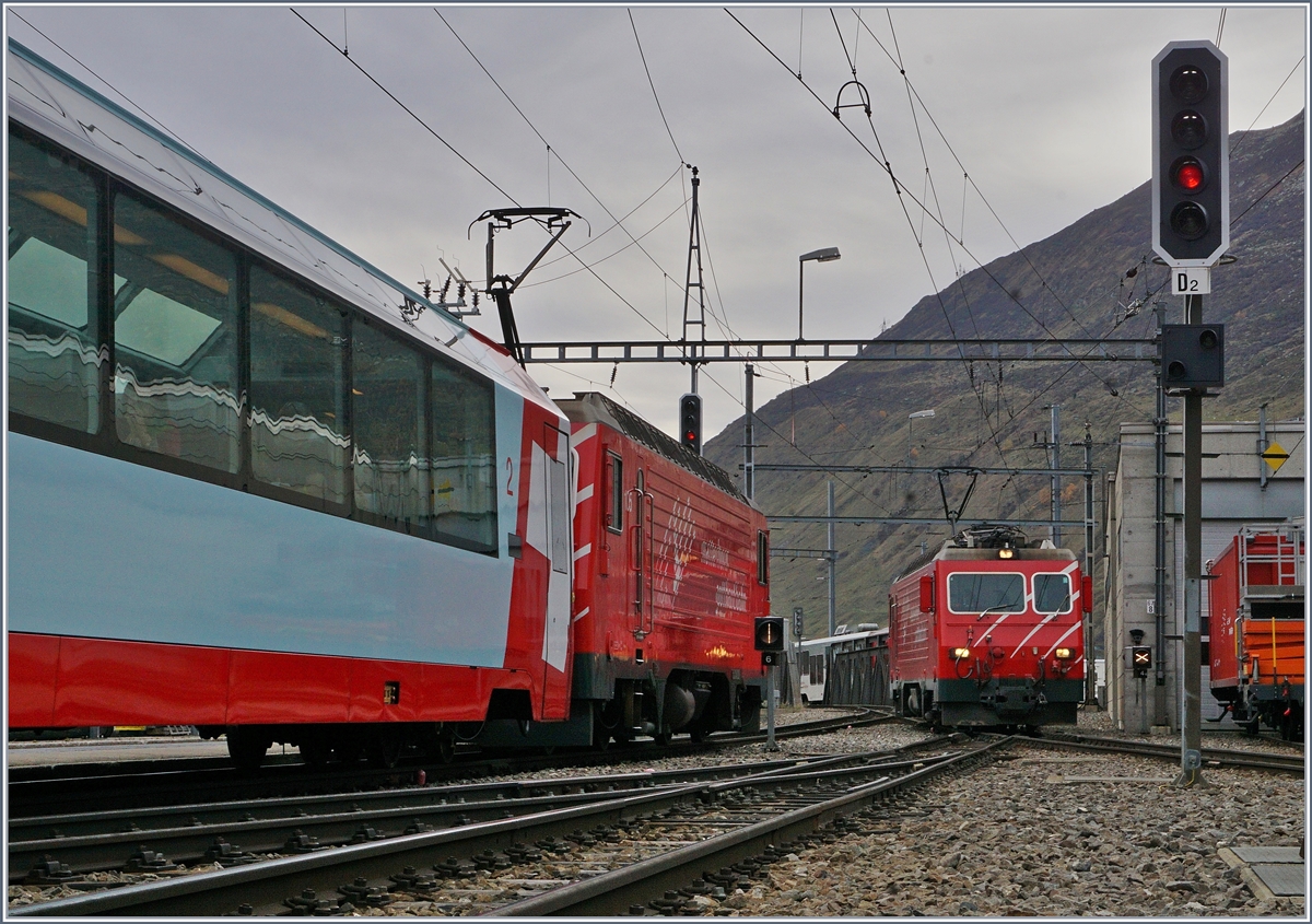 Während die HGe 4/4 des  Disentiser -Zuges in Andermatt rangiert, bzw. ihren Zug umfährt, wartet eine weiter HGe 4/4 mit ihrem Regionalzug 557 auf die Abfahrt nach Visp.
21. Okt. 2017