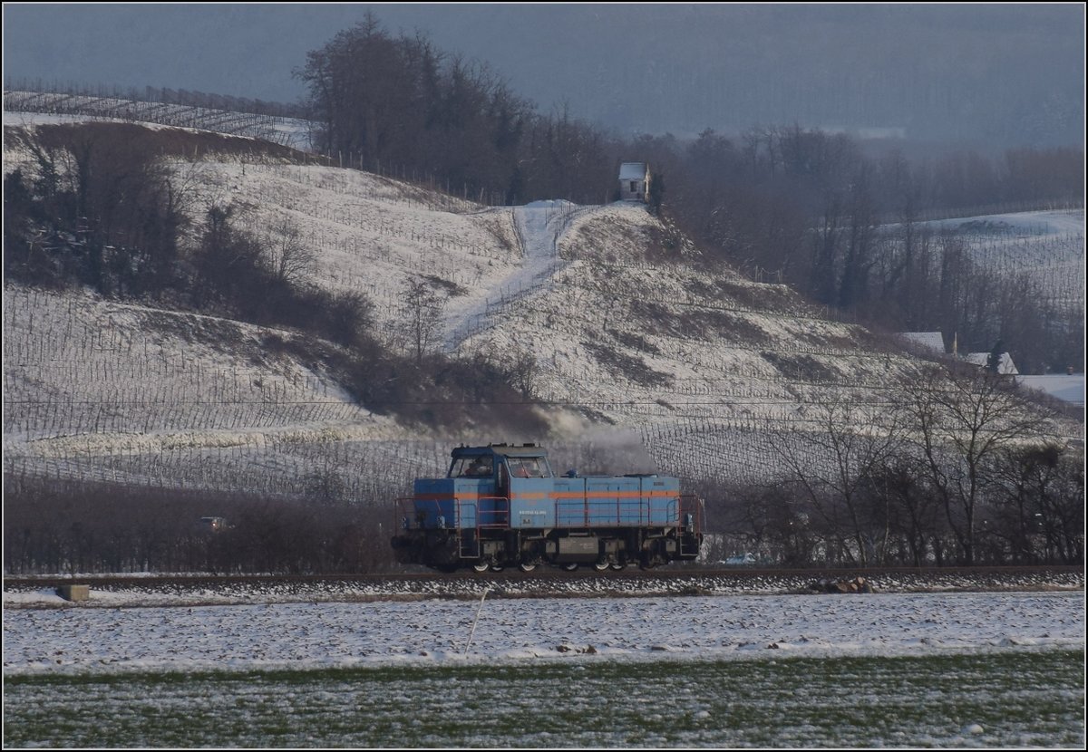 Zwischen Belchensystem und Blauendreieck. 

Eine kleine Lok auf der Magistrale Richtung Basel wird kurz vorher Richtung Neuenburg abbiegen. 0 580 003 der SWEG lässt den Blick auf die Landschaft des Markgräfler Landes völlig frei. Hier blickt man in die Weinberge von Hügelheim und ist gleichzeitig mit der kleinen Gmeinder-Lok in den dunklen Hochnebel abgetaucht. Februar 2021.