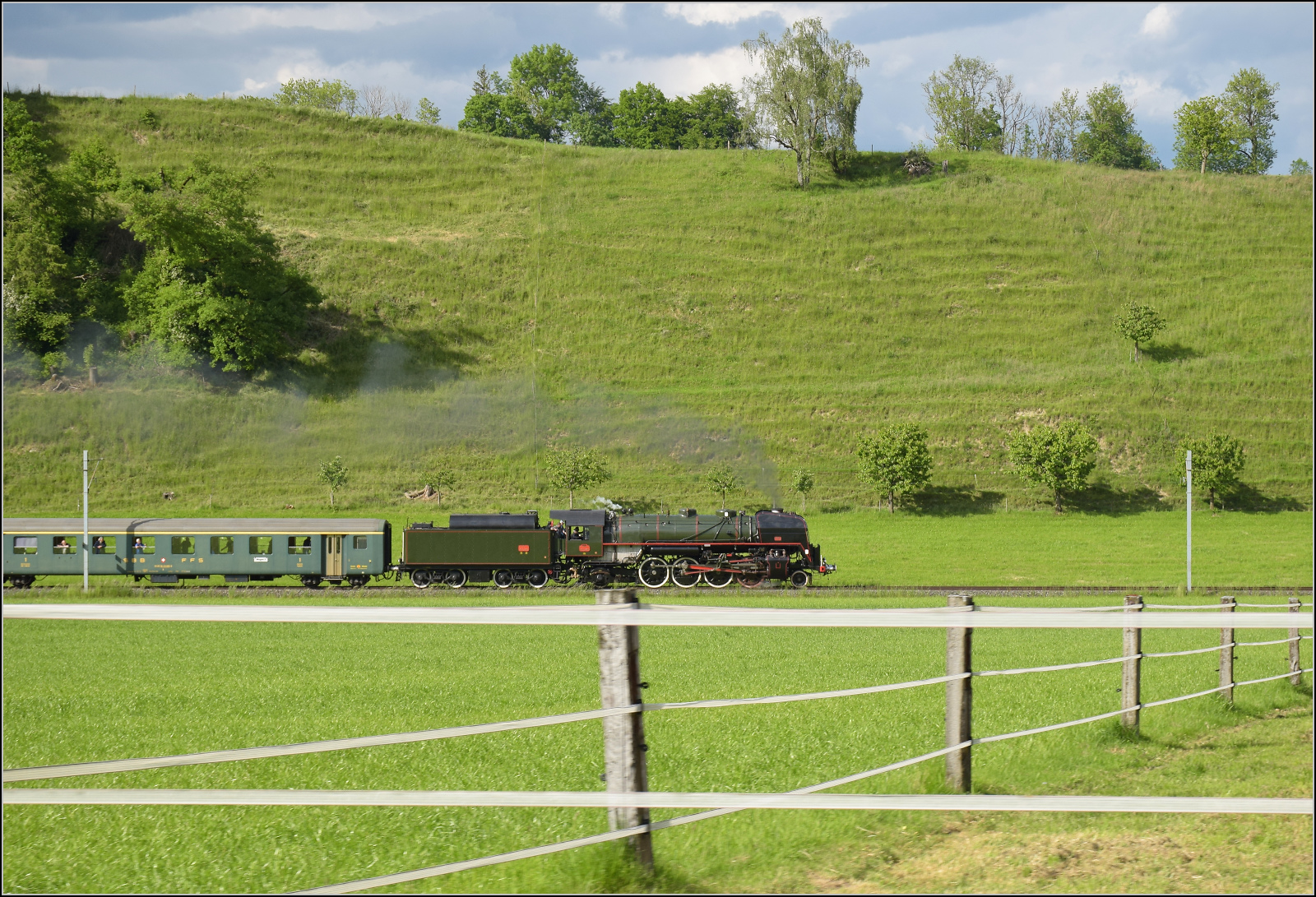 150 Jahre Emmentalbahn. 

141-R-1244 auf dem R�ckweg von der grossen Emmentalrundfahrt anl�sslich des Jubil�ums. Am Ortsausgang Menznau findet die Sonne ein Wolkenloch, freie Sicht auf die Strecke und die Strasse ist ohne Verkehr, perfekt f�r eine Zugverfolgung. Menznau Neuhus, Mai 2025.
