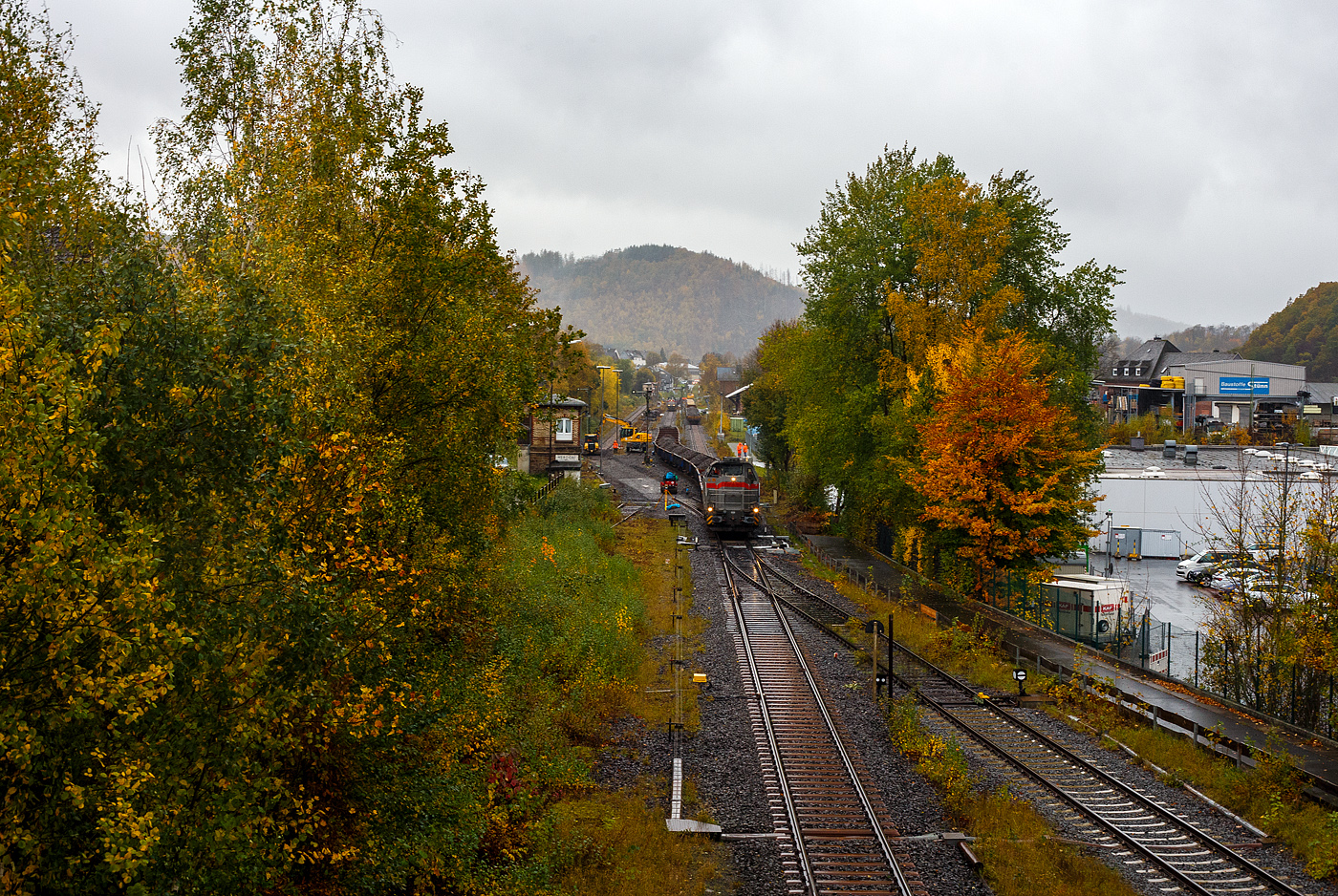 Baustelle Bahnhof Herdorf am 25 Oktober 2025, Blick von der Brcke Wolfsweg („Achenbachs Brcke“) Blickrichtung Betzdorf, es schttete ohne Unterlass, dazu noch heftige Windben, aber die Arbeiten zur Erneuerung der Weiche 3 und der Rckbau mit Lckenschluss fr die drei aufeinander folgenden Weichen 22, 23 und 24 (Erneuerung Anschluss von Weiche 26 an Gleis 4) haben begonnen. So musste ich doch dem widrigen Wetter an die Strecke.

Links ist das alte Gleis und Weichen demontiert und das Gleisbett vorbereitet.

Vorne steht die Vossloh G 12 – 4120 001-7 „Karl August“ (92 80 4120 001-7 D-KAF) der KAF Falkenhahn Bau AG mit einem Schotterzug. Hinten ist die 271 022-6 „Charlotte“ (92 80 1271 022-6 D-KAF) eine Vossloh/MaK G 1000 BB der KAF Falkenhahn Bau AG. ex MRCE bzw. ex HGK DH 49, mit einigen Flachwagen.

Bei dem Wetter haben die Gleisbauarbeiter mein vollstes Mitgefhl. Da haben es die Lokfhrer und Baggerfahrer durch den Schutz ihrer Kabine schon besser. 
