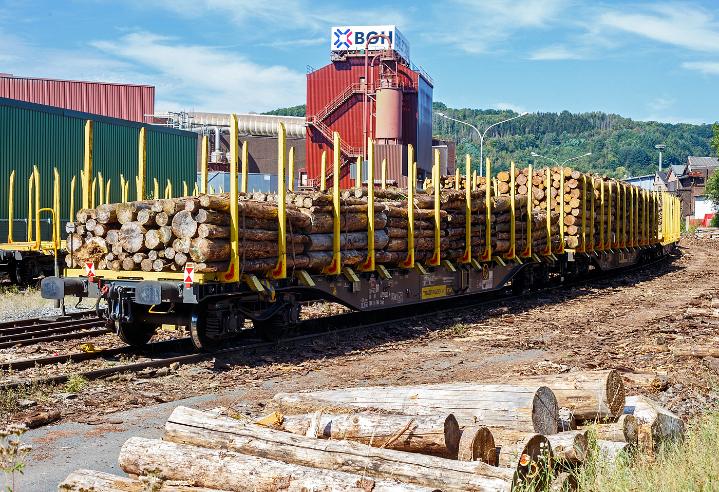 Beladener vierachsiger Drehgestell-Flachwagen (Holzwaggon) mit Niederbindeeinrichtung (Ladungssicherungssystem „Autonordic“) und Rungensystem ExTe (SR8), 81 80 4723 525-9 D-TWA, der Gattung Snps (TWA Bezeichnung SNPZ), der TRANSWAGGON GmbH (Hamburg) zurzeit an die Mercer Holz vermietet, beladen mit Fichten-Rundholz abgestellt am 07 September 2024 in Siegen-Eintracht auf der Gleisanlage der KSW - Kreisbahn Siegen-Wittgenstein (Eisern-Siegener Eisenbahn NE 437).

Der Wagen wurde 2022 von Tatravagonka Poprad (Slowakei) unter der Fabriknummer 013 gebaut (die Drehgestelle unter Fabriknummer 297016).

Die 4-achsigen Wagen Snps sind zum Transport von Holz der Längen 2 m, 2,5 m, 3 m, 4 m, 5,1 m und 6 m bestimmt. Die Wagen sind mit ExTe Ladungssicherungs- und Rungensystem (ExTe SR8) vom schwedischen Hersteller ExTe Fabriks AB in Färila (Schweden) ausgestattet. Die ExTe liefert Produkte an Holzspediteure in der ganzen Welt, die Anforderungen an die Sicherheit auf Straße und Schiene, ein gutes Arbeitsumfeld und einen rationellen Transport stellen. Für die TWA wurden (über die Tatravagonka Poprad) zwischen 2015 und 2022 für 409 dieser Drehgestell-Flachwagen (Snps / SNPZ) diese Systeme geliefert. Wenn man das Rungensystem und die Ladeschwellen entfernt, ist es auch möglich den Wagen für Containertransporte zu verwenden.

TECHNISCHE DATEN des Wagens:
Gattung: Snps (TWA SNPZ, mit Rungensystem ExTe)
Spurweite: 1.435 mm (Normalspur)
Anzahl der Achsen: 4 (in 2 Drehgestellen)
Profil: G2
Länge über Puffer: 20.770 mm
Drehzapfenabstand: 15.230 mm
Radsatzstand in den Drehgestellen: 1.800 mm
Drehgestellbauart: Y25Ls-K (Kopfstückloses Güterwagen-Drehgestell)
Laufragdurchmesser: 920 mm (neu) / 840 mm (abgenutzt)
Ladelänge: 19.530 mm
Fußbodenhöhe über SOK: 1.120 mm UK Ladeschwellen/Rungen (+ 150 mm)
Höhe der Ladeebene: 1.270 mm
Ladequerschnitt: 6,3 m²
Rungenhöhe: 2.488 mm
Ladebreite zw. den Rungen: 2.620 mm
Anzahl der Rungenpaare: 12
Anzahl der Spanngurte („ExTe Autonordic“): 10
Eigengewicht: 23.000 kg 
Max. Zuladung: 67 t (ab Streckenklasse D) 
Max. Geschwindigkeit: 100 km/h (beladen) / 120 km/h (leer)
Kleinster Gleisbogenhalbmesser: 75 m
Bremse: KE-GP-A max. 59 t (K)
Bremssohle: K-Sohle C 810
Feststellbremse: Ja
Intern. Verwendungsfähigkeit: TEN CW

Bedeutung der Gattungsbezeichnung (Snps) :
S = Flachwagen mit Drehgestellen in Sonderbauart
n = Lademasse bei Lastgrenze C: m > 60 t
p = ohne Borde
s = beladen zugelassen für Züge bis 100 km/h

Zudem verfügen diese Wagen der TWA über PJM WaggonTracker ADV:
Die digitale Welt eröffnet viele Möglichkeiten und verschafft vor allem Transporteuren enorme Vorteile. PJM hat die notwendige Verknüpfung zwischen Gütertransporten im Schienenverkehr und der Digitalisierung schon vor langer Zeit erkannt und ist mit dem patentierten Monitoring-System WaggonTracker Pionier. WaggonTracker kombiniert Monitoring und Automation und bietet damit ein robustes Gesamtsystem, das dem Flottenbetreiber enorme Effizienz und Kosten-Einsparungen verschafft: Man erhält wichtige Informationen in Echtzeit über die Fahrzeugflotte und aufwändige Prozesse werden automatisiert.

Der WaggonTracker ADV ist Energieautark, ein Radnabengenerator versorgt die WaggonTracker-Plattform autonom mit Strom. 

Der WaggonTracker übermittelt die Echtzeit-Lokalisierung via Web-Service, u.a. über die Fahrleistung, die aktuelle Position und Radsatz-Laufleistungs-Verwaltung.  Das ADV-System (wie hier) bietet zusätzlich die Überwachung des Fahrzeugzustands, einzelner Komponenten und der geladenen Güter. Im Anlassfall werden Alarmmeldungen verschickt. Es werden z.B. die Achslager-Temperatur und Beladezustand überwacht. Eine Signalisierung / akustische Warnung bei Überladung (asymmetrische Beladung, Radsatzlast) werden bei Ladevorgängen direkt am Wagen signalisiert. Was hier bei solchen Wagen sicherlich für die Holzverladung sehr hilfreich ist. 

Die Signallampen am Wagen zeigen an:
    Überladung
    Radsatzüberlast
    Radscheibenüberlast
    Asymmetrische Beladung
    Unzulässige Drehgestell-Lastverteilung
    Ladung in Ordnung
    Beladungsschwellwert

Automatische Bremsprobe: 
Eine automatische Bremsprobe ersetzt die aufwändige, händische Überprüfung. Bei einem 500 m langen Güterzug bedeutet das eine Zeitersparnis von 30 Minuten. Die Ergebnisse der automatischen Bremsprobe werden auf dem Display des Zugführers oder Bremsproben-Verantwortlichen übersichtlich angezeigt.

Die MERCER Holz:
Mercer Holz ist die Holzeinkaufsorganisation für alle deutschen Produktionsstandorte von Mercer International (Mercer Rosenthal, Mercer Stendal, Mercer Torgau und Mercer Timber Products). Seit mehr als 15 Jahren beliefert sie Zellstoff- und Sägewerke mit großen Industrieholz- und Hackschnitzelmengen. Neben der Belieferung der deutschen Mercer-Werke bietet sie zudem kompetente Beschaffungs-, Holzernte- und Logistikdienstleistungen für Drittkunden an. 

Die Mercer Holz ist auch ein gefragter Dienstleister für die Waldbesitzer. Sie kaufen Holz ein, bündeln es nach Baumarten und Qualitäten und beliefern eigene und dritte Unternehmen gemäß ihrer jeweiligen Ansprüche an Qualität und Logistik. Auf diese Weise kann sowohl für Lieferanten als auch Kunden eine maximale Wertschöpfung bei der Holzaushaltung erzielt werden.
