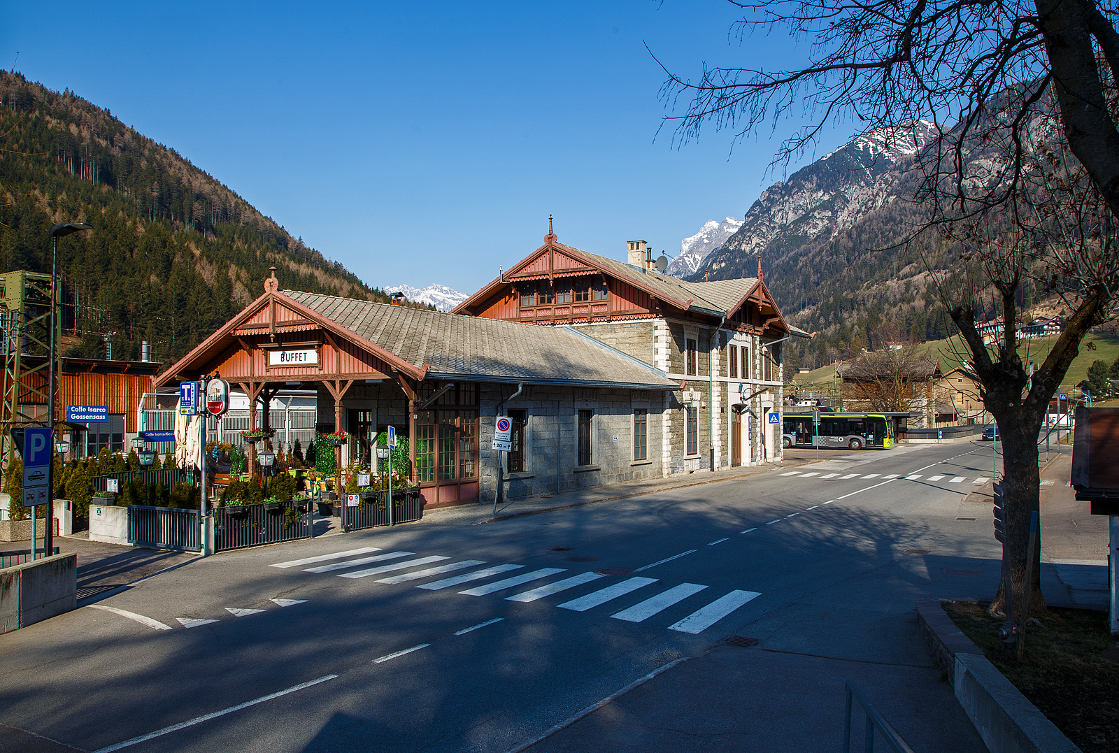 Blick auf den Bahnhof Gossensaß/Colle Isarco am 26.03.2022.
Der Bahnhof Gossensaß (auch Gossensass; italienisch Stazione di Colle Isarco) befindet sich an der Brennerbahn in Südtirol (italienisch Alto Adige), amtlich Autonome Provinz Bozen – Südtirol.

Der Bahnhof Gossensaß ist der erste Haltepunkt im Wipptal südlich des Brennerpasses, zu dem die Bahnstrecke von hier aus über den Pflerschtunnel ansteigt. Er liegt auf 1.066,9 m Höhe nahe dem Zentrum von Gossensaß, dem Hauptort der Gemeinde Brenner, und der durch das Dorf führenden SS 12 (der alten Brennerpass-Straße). 

Der Bahnhof wurde 1867 zusammen mit dem gesamten Abschnitt der Brennerbahn zwischen Innsbruck und Bozen in Betrieb genommen. Durch ihn erlebte Gossensaß bis zum Ersten Weltkrieg seine Blütezeit als bekannter Touristenort. Er konkurrierte mit Orten wie St. Moritz oder Chamonix. 

Das Aufnahmegebäude war zunächst noch relativ kompakt gehalten, wurde wegen der vielen Touristen jedoch noch im 19. Jahrhundert durch einen südlichen Anbau erweitert. Das ursprüngliche Gebäude weist eine Verkleidung aus Grauwacke auf, während dekorative Details wie die Fensterfassungen in weißem Kalkstein gehalten sind. Straßenseitig ist es durch einen in sorgfältigen Details gearbeiteten Dachgiebel aus Holz gestaltet. Der Anbau ist in Brixner Granit gemauert und sticht durch eine hölzerne Veranda hervor. In dem sich heute das Buffet befindet und man auch den Espresso genießen kann. Das Gebäude steht seit dem Jahr 2000 unter Denkmalschutz.

Der Bahnhof Gossensaß wird durch Regionalzüge der Trenitalia sowie der SAD bedient, die auch Busverbindungen zum Bahnhof betreibt. Die Regionalzüge fahren in beide Richtung (Brenner bzw. Bozen) im Stundentakt und werden zu Hauptverkehrszeiten durch Regionalexpresszüge verdichtet.

Uns hat es in Gossensaß sehr gut gefallen, es war einfach zu kurz, so dass wir gerne wiedermal dort hinfahren wollen. Für die drei Tage haben wir uns ein Südtirol/Alto Adige Ticket (eine Mobilcard für 3 Tage) am Automat für 23,00 Euro geholt. So konnten wir mit diesem Ticket Südtirol mit der Bahn erkunden. 