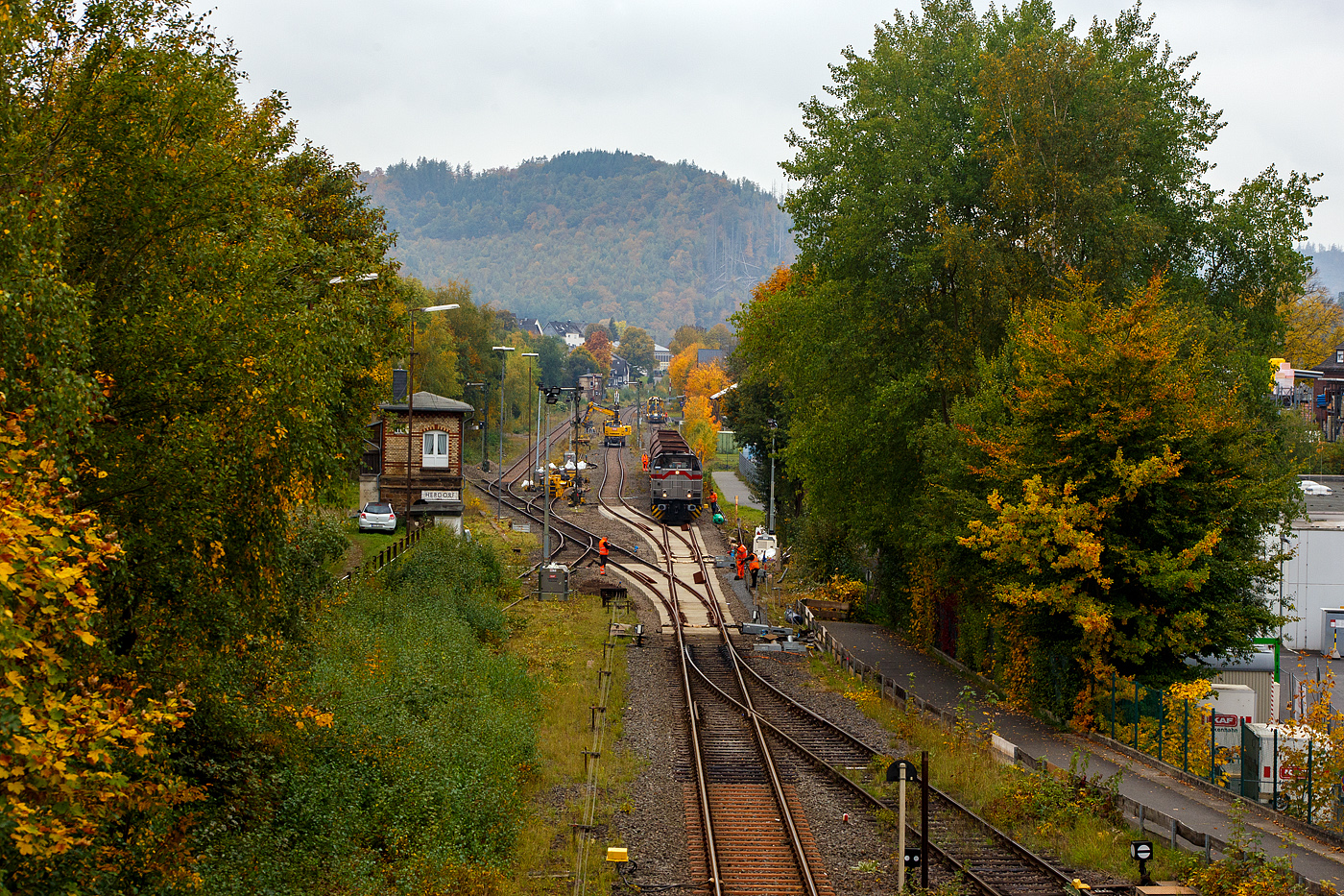 Blick auf den Bahnhof Herdorf und die Baustelle in Blickrichtung Betzdorf am 12 Oktober 2025. Die Weichen 25 und 26 sind beide eingebaut, müssen noch eingeschottert werden.

So steht die 277 809-0  Elmi“ (92 80 1277 809-0 D-KAF), eine Vossloh MaK G 1700 BB der KAF - Falkenhahn Bau AG (Kreuztal), steht mit einem Schotterzug bereit. Hinten beim Bahnhof haben die Schnellschotterplaniermaschine SSP 110 SW, Schweres Nebenfahrzeug Nr. 99 80 9425 068-0 D-DGU und die Universalstopfmaschine UNIMAT 09-475/4S, Schweres Nebenfahrzeug Nr. D-DGU 99 80 9424 001-2, den Bahnhof erreicht müssen aber nach das Einschottern abwarten. Beide Plasser & Theurer Maschinen gehören der Deutsche Gleisbau Union GmbH & Co. KG (DGU), Koblenz

Hier sieht man außerdem gut das Herdorf immer noch den Luxus von 2 Stellwerken besitzt. Vorne links das Weichenwärter Stellwerk Herdorf Ost (Ho) und hinten das Stellwerk Herdorf Fahrdienstleiter (Hf). Beide Stellwerke waren sogar hier bei der Baustelle ganztäglich besetzt.

Ich denke das bei den heutigen Verhältnissen im Bahnhof Herdorf, mit drei aktiven Gleisen und einer Anschlussstelle zum Rangierbahnhof der KSW Kreisbahn Siegen-Wittgenstein (Betriebsstätte FGE - Freien Grunder Eisenbahn) nicht mehr zeitgemäß ist. Es gibt mit Sicherheit heute Möglichkeiten die Aufgaben von einem oder dem anderen Stellwerk fernzusteuern. Früher mit bis zu 30 Gleisen und 3 Anschlussstellen musste es so sein, aber im heutigen Zustand
