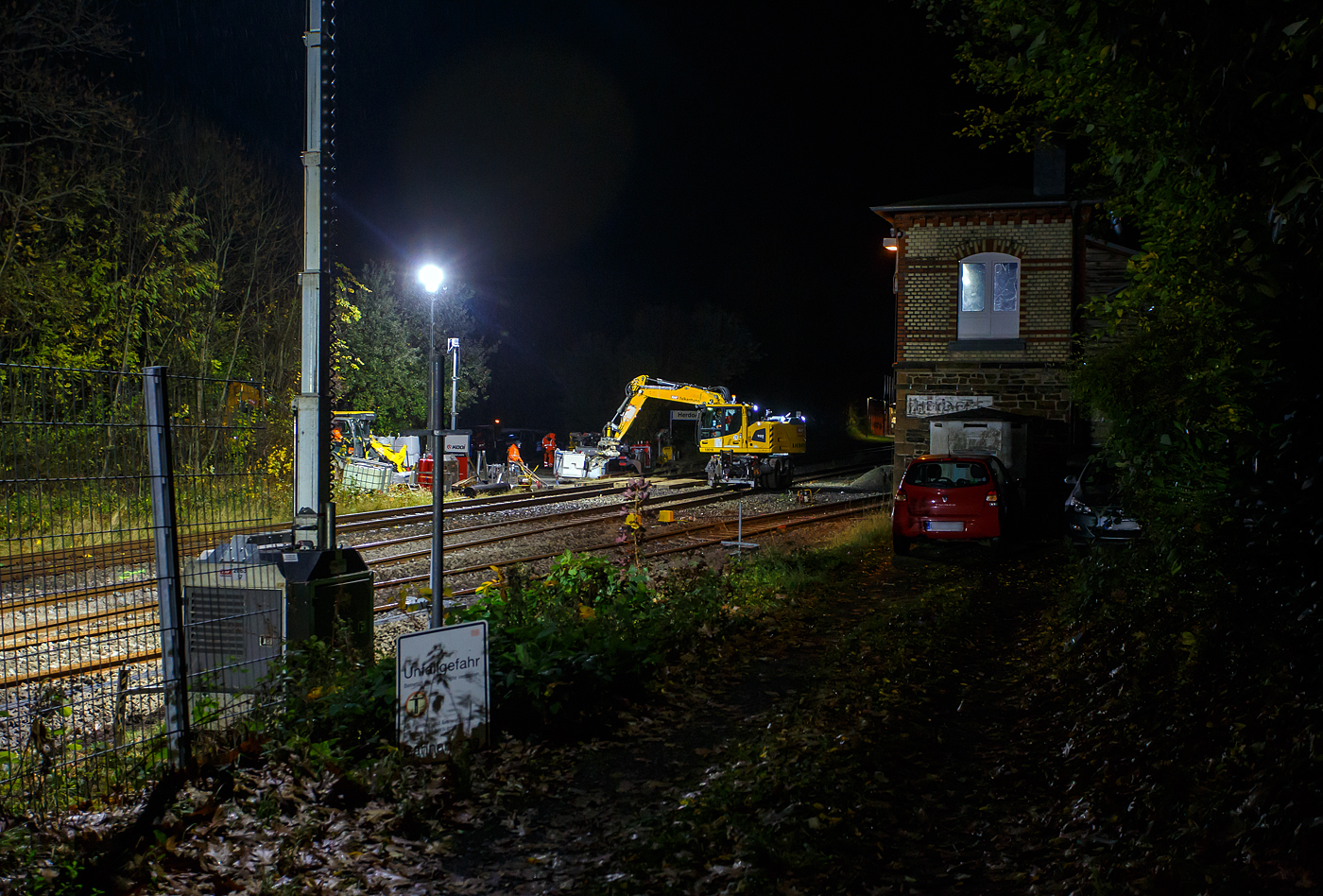 Blick auf die Baustelle Bahnhof Herdorf am Abend des 26 Oktober 2025 (21:30 Uhr). Der Liebherr Zweiwegebagger A 922 Rail Litronic mit Absttzpratzen, Kleinwagen Nr. D-KAF 99 80 9904 795-8 (KAF Interne Nr. 10016), der KAF Falkenhahn Bau AG (Kreuztal), rumt schonmal die Baustelle. Zwischen den Gleisen gelagertes Material wird auf den Lagerplatz gehoben, wo es dann einem Radlader an entsprechende freie Stellen umgesetzt wird.  