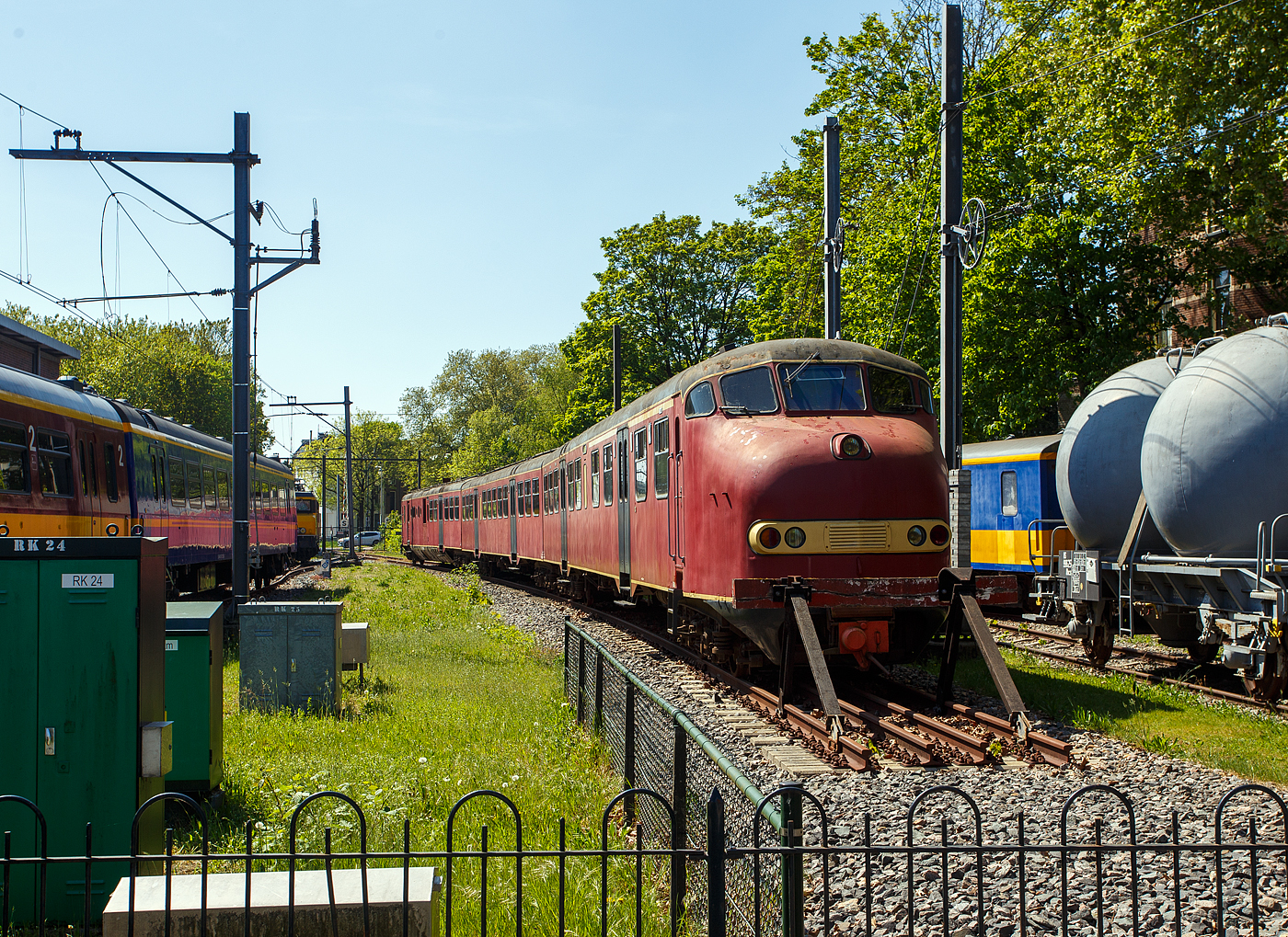 Der dreiteilige Dieseltriebzug NS 114, vom NS-Typ DE 3 – Plan U „Rode Duivel“ (Roter Teufel), am 29 April 2025 im Het Spoorwegmuseum (bis 2005 NSM - Nederlands Spoorwegmuseum / Niederländischen Eisenbahnmuseum) in Utrecht im Bahnhof Maliebaanstation. Ein sehr schönes Eisenbahnmuseum das zum Verweilen einlädt, leider fehlte uns dieses Mal die Zeit dafür. 

Der dieselelektrische Triebzug wurde 1960 von Werkspoor N.V. in Utrecht (NL) für die NS - Nederlandse Spoorwegen (Niederländische Staatsbahnen) gebaut und geliefert. 

Ab 1960 wurden gemäß dem Investitionsplan U der NS 42 dieselelektrische Triebzüge der Serie 111 bis 152 in Betrieb genommen, die die älteren dreiteiligen Dieseleinheiten (Mat'34 – DE3) aus dem Jahr 1934 ersetzten. Die Farbe war ursprünglich Tomatenrot, daher auch ihr Spitzname „Rode Duivel“ (Roter Teufel), auch wenn später ab 1968 „gelb“ wurden, Die Kopfform mit Nase und hoher Kabine wurde von der Materieel '54 abgeleitet. Je nach Verkehrsangebot konnten bis zu drei DE3-Triebzüge mit den automatischen Scharfenberg-Kupplungen kombiniert werden. Das Erscheinen des DE3 diente auch als Vorbild für den späteren Materieel ’64 und die Motorpostwagen der Baureihen 3001 – 3035. Die Dieselzüge waren für den Einsatz auf den nicht elektrifizierten Hauptstrecken wie Geldermalsen – Dordrecht, Zwolle – Emmen, Nijmegen – Venlo – Roermond und anderen Strecken vorgesehen. 

Die Züge haben eine Länge von 74,4 m, eine Breite von 2,78 m und wiegen 136 Tonnen. Die Zuggarnituren bestehen aus drei Wagenkästen. Die Züge ruhen auf sechs Drehgestellen, so ist die Achsfolge ist Bo'Bo' + 2'2' + 2'2'. In einem der Endwagen (mBDk) ist der Motorraum, so war dieser nur Hälfte für Passagiere zugänglich. Diese Endwagen hat zudem einen Gepäckraum von 9 m² und einer Tragkraft von 1.500 kg. Dieser Gepäckraum ist von außen über eine Schiebetür und vom Passagierraum zugänglich. Ein Zug verfügt über 202 Sitzplätze, aufgeteilt in 24 Plätze der ersten Klasse, 168 Plätze der zweiten Klasse und 10 Klappsitze.

Die dreiteiligen Dieseltriebzügen waren mit einem 16-Zylinder-Viertakt-V- Dieselmotor mit Büchi-Hochdruckaufladung und Ladeluftkühlung des Typs Werkspoor RUHB 1616 ausgestattet. Der Motor mit einer Ricardo-Wirbelkammereinspritzung ausgerüstet. Der Motorhubraum betrug 64,339 Liter (4,021 Litern je Zylinder, Bohrung Ø 160 mm x 200 mm Hub). Die Motorleistung betrug 1.000 PS (736 kW) bei 1.400 U/min, die Leerlaufdrehzahl lag bei 800 U/min. Dieser Dieselmotor trieb einen direkt gekuppeltem Hauptgenerator vom Typ Heemaf GMT 1040 an. Dieser Generator liefert eine Leistung von 625 kW bei einer Spannung von 700 Volt. Der erzeugte Strom treibt die 4 Vickers AEI-Traktionsmotoren vom Typ MV 139, oder Heemaf Typ GT 38-22 (mit gleichen Spezifikationen), an. Jeder E-Motor hat eine Leistung von 147 kW (PS) bei 700 Volt. Der Zug verfügt so über eine Gesamttraktionsleistung von 588 kW am Rad. Die Aufhängung dieser Motoren entspricht der Aufhängung einer Straßenbahn. Der Fahrmotor ruht auf einer Seite auf einem Stahlgussrohr, welches mit zwei Kegellagern auf der Achse gelagert ist. Das Motorgehäuse wird mit zwei Deckeln auf das Stahlgussrohr gummigelagert geklemmt. Der Antrieb der Motorwelle erfolgt über ein Ritzel, das ein Zahnrad auf der 
Radwelle antreibt. Das Übersetzungsverhältnis beträgt 17:65. Der Zug ist für eine Geschwindigkeit von 140 km/h ausgelegt, im Planbetrieb wurde eine Geschwindigkeit von 125 km/h gefahren. Zur Stromversorgung des Steuerstroms und der Beleuchtung sind am Hauptgenerator ein Generator und ein Hilfsgenerator der Firma Heemaf, Typ GMT 370/20, installiert. Der Antrieb erfolgt mittels Keilriemen. Mit einer Leistung von 30 kW liefert der Hilfsgenerator 145 Volt für Wechselrichter, Steuerstrom und Kabinenheizung. 

Der Triebzug ist mit einem Kraftstofftank mit einem Fassungsvermögen von 1.675 Litern ausgestattet. 

Ab 1968 wurden die Züge in der neuen NS Hausfarbe Gelb lackiert. Ab 1972 wurden die Schiebetüren durch die inzwischen von Mat ’64 eingeführten und erfolgreich erprobten Pendeltüren ersetzt. Lediglich die Schiebetür im Gepäckraum blieb erhalten.

1980 begann man damit die Werkspoor Dieselmotore gegen einen V-12-Zylinder-Viertakt-Dieselmotor mit Abgasturboaufladung und Ladeluftkühlung vom Typ MGO-175 BSHR vom französischer Hersteller SACM (Société Alsacienne de Constructions Mécaniques mit Sitz in Mulhouse, Elsass). Der Motorhubraum betrug nun 53,7 Liter (Bohrung Ø 180 mm x 175 mm Hub). Die Motorleistung betrug nun 1.430 PS (1.050 kW) bei 1.500 U/min. Dieser Austausch wurde notwendig, da Werkspoor 1977 die Herstellung von Teilen für den RUHB-Dieselmotor einstellt. Die Ersatzteilversorgung wurde bereits 1976 problematisch. Um genügend Motoren zur Verfügung zu haben, wurde ein neuer Lieferant gesucht und die Motoren von SACM. Neben dem Austausch des Dieselmotors wurde auch das Kühlsystem modifiziert. Durch den Motorentausch konnten 15 % Kraftstoff gespart werden und die neuen Motoren machten weniger Lärm.

TECHNISCHE DATEN:
Serie: NS DE 3 – Plan U „Rode Duivel“ (Roter Teufel)
Gebaute Anzahl: 42
Nummerierung: 111-152 (191-195)
Typ: dieselelektrischer Triebzug
Baujahre: 1960-1963
Ausmusterung: 2003
Hersteller: Werkspoor N.V. in Utrecht
Spurweite: 1.435 mm (Normalspur)
Achsfolge: Bo'Bo' + 2'2' + 2'2' (12 Achsen in 6 Drehgestellen)
Zusammensetzung: mBDk + B + ABk
Länge über Kupplung: 74.430 mm
Breite: 2.780 mm
Höhe: 3.770 mm
Treib- und Laufraddurchmesser: 950 mm (neu) 
Dieselmotor: 16-Zylinder Werkspoor RUHB 1616, ab 1980 12-Zylinder 
SACM MGO-175 BSHR (Beschreibungen s.o.)
Motorleistung: 736 kW (1.000 PS)
Übersetzung: 17:65
E-Antriebsmotoren: 4 Stück Vickers Typ MV 139 oder Typ GT 38-22 
E-Motordauerleistung: 4 x 147 kW = 588 kW
Höchstgeschwindigkeit: 125 km/h (Planmäßig) / 140 km/h (Konstruktiv)
Eigengewicht: 136 t 
Anzahl der Doppeltüren je Seite: 6
Sitzplätze (gesamt): 202
Sitzplätze in der 1. Klasse: 24
Sitzplätze in der 2. Klasse: 168
Anzahl der Klappsitze: 10
Gepäckraum: 9 m² mit 1.500 kg Nutzlast
Tankvolumen: 1675 Liter
Kupplung: Scharfenberg
