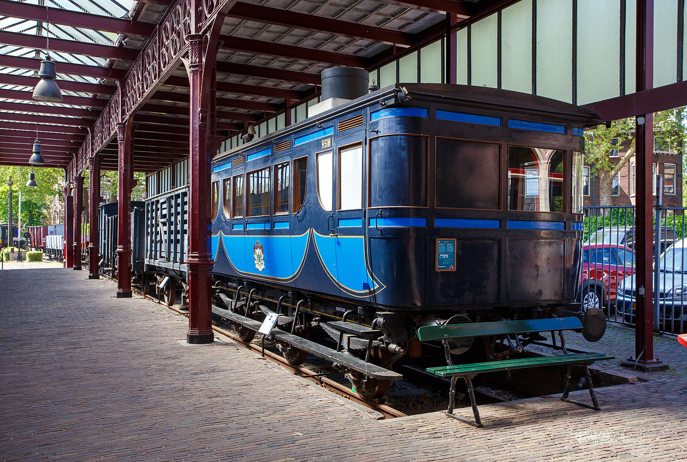 Der königliche Salonwagen HSM Sr 1 (Replikat) am 29 April 2025 im Het Spoorwegmuseum (bis 2005 NSM - Nederlands Spoorwegmuseum / Niederländischen Eisenbahnmuseum) in Utrecht im ehemaligen Bahnhof Maliebaanstation.

Der ursprüngliche Salonwagen Nummer 1 (Sr 1) wurde speziell für Anna Paulowna von Holstein-Gottorp-Romanow, Großfürstin von Russland und Witwe von König Willem II. (Wilhelm Friedrich Georg Ludwig von Oranien-Nassau), von 1840 bis 1849 König der Niederlande und in Personalunion Großherzog von Luxemburg, die selbst darauf bestand, gebaut. Sie wollte mit ihrem eigenen Wagen von Soestdijk nach Den Haag fahren können. Der Sr 1 war einer der ersten königlichen Wagen (Royal Wagen) und wurde 1864 in der Haarlemer HSM-Werkstatt gebaut. Am 21. November 1864 wurde der noch nummerierte Wagen inspiziert und für in Ordnung befunden. Bis zur ministeriellen Genehmigung vergingen mehrere Wochen. Im Winter zog die königliche Gesellschaft den warmen Kamin einer Zugfahrt vor, die nur mit Öfen beheizt wurde. Anna Paulowna hat ihn nie benutzt, da sie noch vor der Indienststellung des Wagens am 1. März 1865 nach mehrwöchiger Krankheit in Den Haag verstarb. Der Wagen wurde aber regelmäßig von Prinz Frederik, dem jüngeren Bruder von König Wilhelm II., genutzt.

Der zweiachsige Sr 1 wurde mehrfach modifiziert. Er war für Breitspur (1.945 mm) gebaut worden, doch 1864 beschloss die HSM (bzw. HIJSM) - Hollandsche IJzeren Spoorweg-Maatschappij (Niederländischen Eisenbahn-Gesellschaft), die Gleise auf Normalspur (1.435 mm) umzubauen. Erst wurde neben dem eingleisigen Breitspurgleis, auf der gesamten Strecke Amsterdam – Haarlem – Den Haag – Rotterdam. ein zweites Gleis in Normalspur (1.435 mm) verlegt, um auch in Zukunft den Anschluss an das übrige Europa nicht zu verpassen. Dieses eingleisige Normalspur-Gleis wurde am 2. Mai 1866 fertiggestellt.

Der Innenraum des Wagens wurde 1884 vollständig renoviert, im Zuge der Renovierung wird der Waggon auch mit einer Toilette und einem Waschbecken ausgestattet. Die Sr 1 des Eisenbahnmuseums ist ein Nachbau aus dieser Zeit. Das Replikat wurde 2010 von Kloosterboer in Purmerend speziell für das Museum gebaut. Toilette und Waschbecken sind original, dies sind die einzigen Originalgegenstände, die erhalten geblieben sind. Anschließend wurde die Karosserie des Salonwagens auf ein neues dreiachsiges Normalspur-Fahrgestell gesetzt. Zum ersten Mal wurde ein neuer Radtyp verwendet, bestehend aus sechzehn Teakholzsegmenten um eine Nabe aus Schmiedeeisen, mit einem Radband aus Schmiedeeisen rundherum, System Mansell.

Die Nummer Sr 1 und die Abkürzung HSM erhielt der Wagen erst 1870, als in Den Haag die Verbindungskurve zu den NRS-Strecken eingerichtet wurde und der Verdacht aufkam, dass der Wagen auch auf ausländischen Strecken gefahren werden könnte.

Nachdem Prinz Frederik 1881 im Alter von 84 Jahren starb, wurde der Salonwagen kaum noch genutzt. Die HSM gab dem Wagen deshalb im Jahr 1884 eine andere Bestimmung. Ein Teil eines Endabteils wurde abgetrennt und mit einer Toilette und einer Waschgelegenheit versehen. Anstelle einer Ölbeleuchtung war der Wagen mit einer Gasbeleuchtung ausgestattet. Die Öfen wurden durch eine Brikettheizung ersetzt. Der Wagen wurde dann Menschen zur Verfügung gestellt, die es sich leisten konnten, den harten niederländischen Wintern zu entfliehen. Also VIP-Wagen „avant la lettre“.

Im Jahr 1905 nutzte die damalige Königin Wilhelmina nutzte den Wagen noch einmal für einen Besuch in der Provinz Friesland. 1908 wurde der Sr 1 außer Dienst gestellt und verschrottet.

Im Jahr 2009 beauftragte das Eisenbahnmuseum die Firma Kloosterboer in Purmerend mit dem Bau einer Nachbildung des Sr 1. Der Waggon, dessen Bau von der Bank-Giro-Loterij gesponsert wurde, spielte 2010 eine Hauptrolle in der Ausstellung „Royal Class“.

TECHNISCHE DATEN (Replikat)
Hersteller: Fa. Kloosterboer Decorbouw, Purmerend
Baujahr: 2010
Spurweite:1.435 mm
Anzahl der Achsen: 3
Länge über die Puffer: 8,76 m
Gewicht: 12,84 t
Betriebsfähig: nein