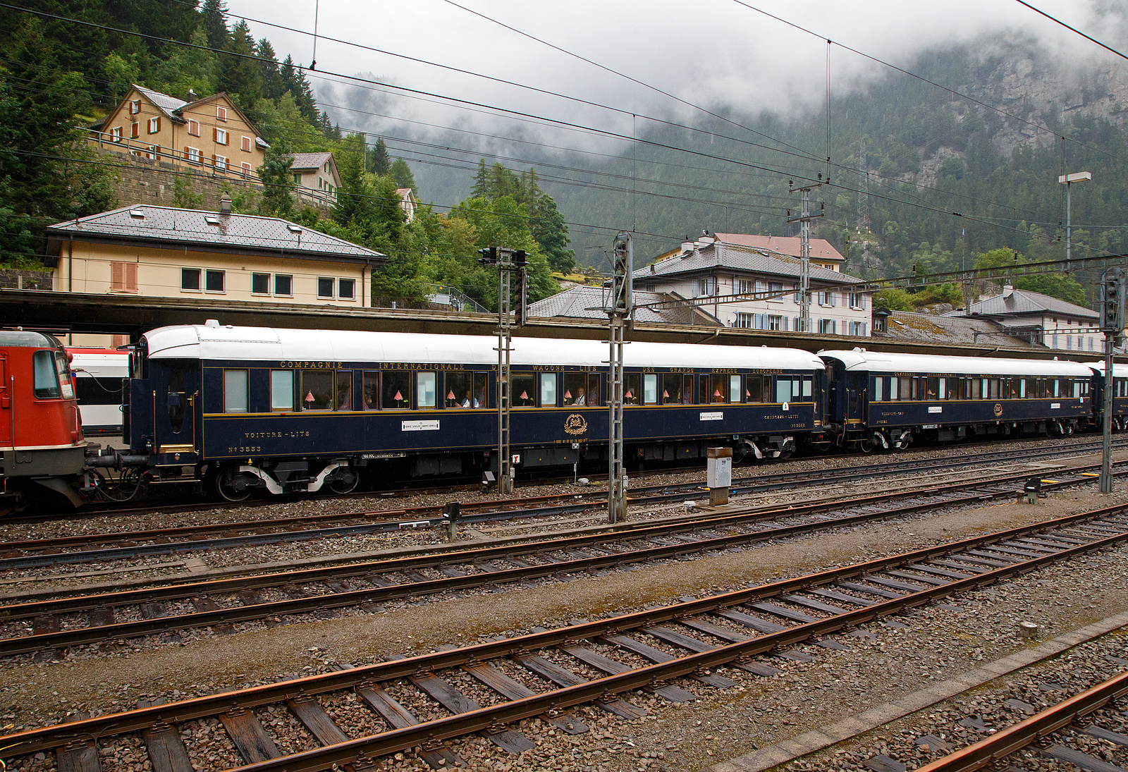 Der VSOE Schlafwagen Nr. 3553 – VSOE Voiture-Lits / Carrozza-Letti N� 3553 (F- VSOE 61 87 06-70 553-9 [P]) im Zugverbund vom Venice Simplon-Orient-Express am 02.08.2019 beim Halt im Bahnhof G�schenen (CH), leider bei Regen.

Der Schlafwagen, wurde 1929 von EIC - Entreprises industrielles des Charentes (EIC, heute zu Alstom geh�rend) in Aytr� (F), als CIWL Typ Lx 18 (Schlafwagen mit Schlafwagenschaffnerabteil), gebaut und als Schlafwagen Nr. 3553 an die CIWL - Compagnie Internationale des Wagons-Lits geliefert. 1943 wurde er zum in den Typ LX 20 (zehn Zweibettabteile) umgebaut. Im Jahr 1980 wurde er an die VSOE (Venice Simplon-Orient-Express Ltd.) verkauft. Hier wurde der Wagen �berholt und technisch modernisiert, unter anderem mit Klimaanlagen. Bei den VSOE-Wagen wurde ein Schlafwagenabteil zum Abteil f�r den Schlafwagenschaffner hergerichtet, die Wagen werden seitdem (wieder) als Typ Lx 18 bezeichnet. 

Zwischen 2003 und 2006 wurde die Wagen der VSOE wieder modernisiert und erhielten unter anderem moderne Drehgestelle von Bombardier sowie neue Klimaanlagen. Durch die neuen Drehgestelle sind die Wagen seitdem f�r 160 km/h zugelassen. 

TECHNIK
Mit der Einf�hrung von Ganzstahlwagen ging die CIWL dazu �ber, von Ausnahmen abgesehen alle Fahrzeuge auf einem einheitlichen Rahmen mit 23.452 mm L�nge �ber Puffer und einem Drehzapfenabstand von 16.000 mm aufzubauen. Die Fahrzeugbreite betr�gt 2.850 mm, die H�he �ber Schienenoberkante 4.000 mm. Auf dieser Basis entstanden neben dem Typ Lx auch die Schlafwagen der Typen S, Y und Z. Die gleichen Rahmen wurden auch f�r Speisewagen und Pullmanwagen verwendet, sie bestehen aus drei L�ngstr�gern mit Querverbindungen und zwei Gussstahlbl�cken an den Enden zur Aufnahme der Zug- und Sto�vorrichtungen. Auf dem Rahmen sind die Seitenw�nde und Fu�b�den sowie die beiden Zustiegsplattformen aufgebaut. Das Gewicht des Typs Lx bel�uft sich auf 53 Tonnen (heute 57 t). Als Drehgestelle erhielten die Wagen urspr�nglich Schwanenhals-Drehgestelle mit Rollenlagern, auch als Pennsylvania-Drehgestelle bezeichnet. Im Laufe der Jahre wurden diese teilweise durch neuere Drehgestelle oder andere Bauarten ersetzt. Urspr�nglich waren die Wagen lediglich f�r 130 km/h zugelassen, nach dem Krieg wurde die Geschwindigkeit auf 140 km/h angehoben. Die mit neuen Drehgestellen modernisierten Wagen des VSOE sind f�r 160 km/h zugelassen.

Die CIWL r�stete alle Wagen neben einer �ber die Heizdampfleitung des Zuges versorgten Dampfheizung mit einer unabh�ngig zu betreibenden Kohleheizung aus, die durch den Schlafwagenschaffner bedient wurde und bei l�ngerem Stillstand eines Zuges zum Einsatz kam. In den Nachkriegsjahren erhielten viele Fahrzeuge au�erdem elektrische Heizleitungen. In jedem Abteil befand sich zur Bel�ftung ein Ventilator, die Wagen der VSOE wurden mit Klimaanlagen ausger�stet.

Es gab kein gesondertes Abteil f�r den Schlafwagenschaffner, dieser n�chtigte auf einer an einem Ende des Wagens aufgeklappten Liege im Gang. Vorr�te f�r die Versorgung der Fahrg�ste befanden sich in Schr�nken an den Wagenenden. An einem Ende war ein WC untergebracht. Jeweils zwei der Abteile (mit Ausnahme der beiden �u�ersten Abteile) lie�en sich mittels einer verschlie�baren T�r zu einer gr��eren Suite verbinden. Die in den historischen Luxusz�gen eingesetzten, noch erhaltenen Wagen des Typs sind teils umfassend modernisiert und umgebaut worden. Bei den im VSOE eingesetzten Wagen wird eines der Abteile f�r den Schaffner genutzt. Die Wagen besitzen zudem moderne Klimaanlagen.

TECHNISCE DATEN:
Spurweite: 1.435 mm (Normalspur)
Anzahl der Achsen: 4 in zwei Drehgestellen
L�nge �ber Puffer: 23.452 mm
Drehzapfenabstand: 16.000 mm
Achsabstand im Drehgestell: 2.500 mm
Eigengewicht: 57 t
H�chstgeschwindigkeit: 160 km/h (urspr�nglich 140 km/h)
Betten- und Sitzpl�tze: 18 (in 9 Zweibettabteilen) plus Schaffnerabteil 

DER HEUTIGE WAGEN 3553 - L'Observatoire
Im Jahr 2023 entwarf franz�sische K�nstler JR das Innere des neuen Privatwagens 3553 - L'Observatoire (Privatwagen) des Venedig Simplon-Orient-Express, der so 2023/24 umgebaut wurde und nun die UIC-Nummer F- VSOE 61 87 76-70 000-6 [P] tr�gt. Jetzt ist es ein Privatwagen mit einem Schlafzimmer f�r zwei Personen, einem Wohnzimmer, einer Bibliothek, einer Teekammer und einem Badezimmer mit freistehender Badewanne. Das Fahrzeug wurde im April 2024 auf der Biennale in Venedig ausgestellt, um erste Eindr�cke zu liefern, und es l�uft seit 2025 im Zug des Venice Simplon-Orient-Express. Ich w�rde ich gerne mal selbst von innen sehen. 

L’Observatoire, das sich �ber einen ganzen Wagen an Bord des Venedig Simplon-Orient-Expresss entfaltet, ist ein einzigartiger Raum, um Neugier, Abenteuer und Kreativit�t zu genie�en. Inspiriert von astronomischen Observatorien hat der K�nstler JR eine wagengro�e Suite entworfen, er soll ermutigen, zu blicken, hinaus und dar�ber hinaus - und zwar mit Handwerkskunst sowohl von alten Meistern als auch von aufstrebenden Wegbereitern harmonieren. Wenn man das n�tige Kleingeld hat😉.

In einem 23 Meter langen Raum entfalten sich die Innenr�ume des Wagens in mehreren Umgebungen, von einem Schlafzimmer mit einer freistehenden Badewanne bis zu einer Bibliothek voller Gallimard-B�cher. Wenn man den Korridor entlang schlendert, kann man die ausgestellte JR-Fotografie bewundern. Ein Plattenspieler mit einer kuratierten Vinyl-Sammlung ist als Soundtrack zum au�ergew�hnlichen Abenteuer auch dabei.

Zudem hei�t es: Enth�llen Sie handgefertigte Intarsien, Glasmalereien und sogar einen Miniatur-Zugwagen, der von einem Modellbaumeister aus der Schweiz geschaffen wurde. Schauen Sie n�her, um eine Welt von Feiernden zu entdecken, die auf winzigen Bildschirmen im Inneren des Modells laufen. Entdecken Sie die versteckte Teestube, ein kreisf�rmiges Refugium, in dem Sie Momente stiller Kontemplation genie�en k�nnen. Dieser exklusive Raum ist nur f�r Ihre Augen reserviert. Schlie�lich schauen Sie auf, um einen Oculus zu enth�llen und den Himmel zu bestaunen.
