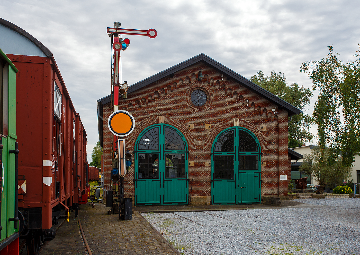 Der zweiständige Lokschuppen Hochdahl am 26 Mai 2024, heute Museum vom Eisenbahn- und Heimatmuseum Erkrath-Hochdahl e.V.

Gebaut wurde er 1864 von der ehemaligen Bergisch-Märkische Eisenbahn-Gesellschaft für die Wartung der Hilfslokomotiven Steilrampe Erkrath–Hochdahl. Es ist noch ein Relikt was aus der Epoche der Privateisenbahnen stammt aus der Zeit. Die Bergisch-Märkischen Eisenbahn (1843-1886). 

Die Strecke, die Verbindung von Düsseldorf nach Elberfeld (heute Wuppertal Hbf) befuhr die erste Eisenbahn in Westdeutschland. Ein Teilstück bis Erkrath wurde bereits am 20.12.1838 in Betrieb genommen. Im weiteren Verlauf war eine für Lokomotiven der damaligen Zeit fast unüberwindliche Steigung zwischen der Rheinebene (Erkrath) und dem beginnenden Bergischen Land (Hochdahl) zu überwinden. Auf ca. 2.500 m Länge war dies ein Höhenunterschied von ca. 82 m. Dies konnte nur mit technischen Meisterleistungen der Ingenieure bewältigt werden. Eine Seilzuganlage, die erst mit einer Dampfmaschine, später allein mit Umlenkrollen betrieben wurde, ermöglichte bis 1926 den Zugbetrieb. Bis 1963 wurde den Dampfzügen mit Vorspann- und Schiebelokomotiven geholfen, die Steilrampe zu überwinden, danach schafften es Elektroloks fast problemlos alleine.

Die Steilrampe Erkrath–Hochdahl ist der 1841 durch die Düsseldorf-Elberfelder Eisenbahn-Gesellschaft in Betrieb genommene Abschnitt der Bahnstrecke Düsseldorf–Elberfeld. Sie liegt zwischen den Bahnhöfen Erkrath und Hochdahl (oben).  Zwischen den beiden Enden der etwa 2,5 Kilometer langen Steilrampe besteht ein Höhenunterschied von 82 Meter, was eine Steigung von 3,3 % (33 ‰) ergibt. Der Streckenabschnitt zählt damit zu den steilsten Hauptstrecken-Abschnitten in Deutschland, während hingegen die restliche Strecke sehr flach verläuft. Somit ist die durchschnittliche Steigung der Gesamtstrecke mit 110 Meter Höhendifferenz auf 27 Kilometer = 4 ‰ sehr niedrig. 

Der Betrieb mit Umlenkrollen:
Schon im Laufe des Jahres 1841 stellte sich das Verfahren mit der Seilzuganlage als unwirtschaftlich heraus. Die Anlage wurde so umgebaut, dass ein zu Tal fahrender Zug einen entgegenkommenden bergwärts fahrenden Zug mit diesem Seil über drei Umlenkrollen die Rampe hinauf zog. Oft wurde auch eine eigens in Hochdahl stationierte Lokomotive für die ziehende Talfahrt eingesetzt. Auf die stationäre Dampfmaschine konnte daraufhin verzichtet werden. Das Maschinenhaus wurde aber erst Anfang der 1980er Jahre abgerissen. 

Betrieb mit Zusatzlokomotiven:
1926 wurde der Seilzugbetrieb durch den Einsatz von Lokomotiven mit ausreichender Leistung überflüssig. Stattdessen wurden ab Erkrath bis zu zwei Schiebe- und vor allem bei schweren Güterzügen zusätzlich Vorspannlokomotiven eingesetzt, so dass bis zu vier Dampflokomotiven mit Anlauf einen Zug den Berg hinaufbeförderten.

Erst seit Elektrifizierung der Steilstrecke 1963 und der Gesamtstrecke 1964 schaffen die Züge ohne weitere Hilfe den Weg hinauf zum Hochdahler Bahnhof. Damit war der Zwangshalt auch aller Schnellzüge in Erkrath vorbei, mit dem man für eine Ansiedlung im Ort warb. 1914 hielten täglich 84 Züge.

Bis in die 1980er Jahre war die Steilstrecke auch für moderne Züge noch eine Herausforderung. Noch 1988 kam es vor, dass Züge, die am Berg halten mussten, nach Erkrath zurücksetzten, um mit neuem Anlauf den Berg zu erklimmen.
