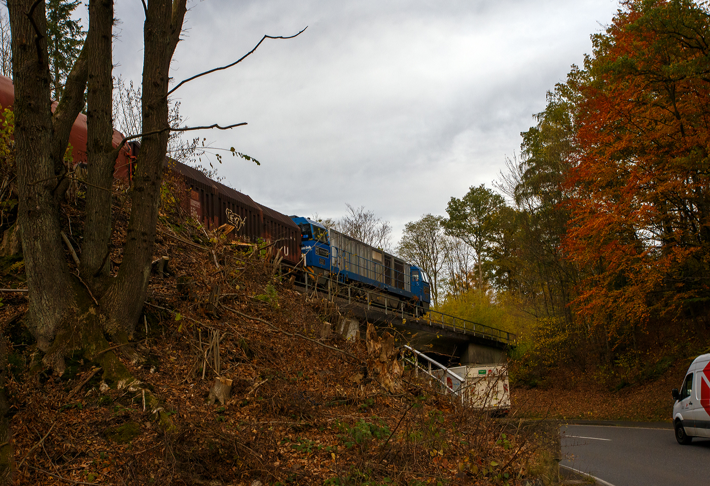 Die an die KSW vermietete 272 409-4 / D21 (92 80 1272 409-4 D-BE) der Bentheimer Eisenbahn, ex Rurtalbahn V 204 (92 80 1272 409-4 D-RTBC), eine Vossloh G 2000 BB (mit symmetrischem Führerhaus), fährt am 31 Oktober 2025 mit ihrem Coilzug zwischen Sassenroth und Herdorf nun gleichdrauf über die erste Brücke Hollertszug.