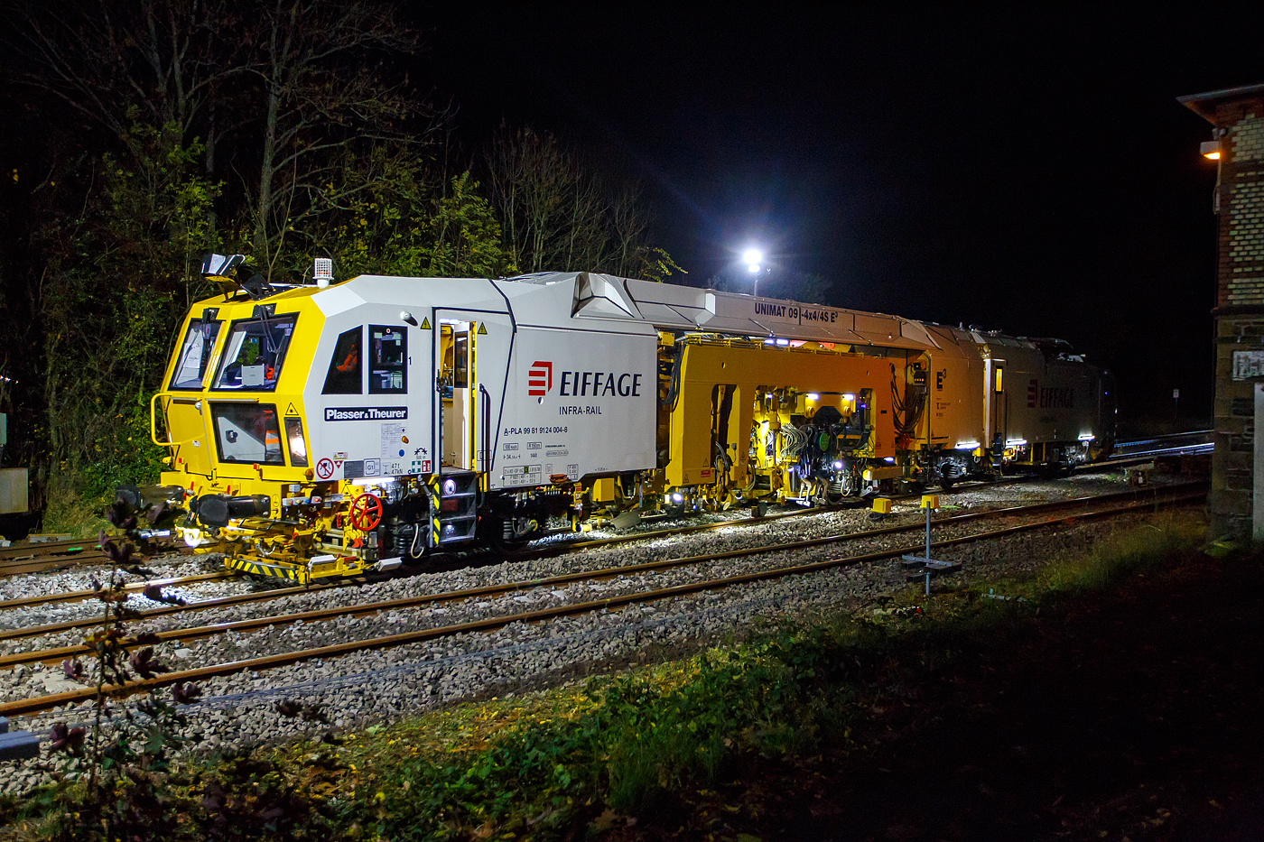 Die Baustelle Bahnhof Herdorf am Abend des 26 Oktober 2025, nun ab 20:40 Uhr wird die neue Weiche 3, beim Bahnhof/Stellwerk Herdorf Fahrdienstleiter (Hf), gestopft. Hier kam die recht neue Plasser & Theurer UNIMAT 09-4x4/4S E (A-PLA 99 81 9124 004-8), eine Universal-Weichenstopfmaschine mit Hybrid-Antriebstechnik, der Firma Eiffage Infra-Rail GmbH (Herne) zum Einsatz. Ob die Maschine nur von Eiffage Infra-Rail gemietet oder nun gekaut wurde ist mir nicht klar, aber eingestellt ist sie in sterreich ber Franz Plasser Vermietung von Bahnbaumaschinen GmbH. 

Die Maschine wurde 2017 von Plasser & Theurer in Linz unter der Fabriknummer 6557/58 gebaut. Diese Maschine mit der neuen E-Antriebstechnologie von Plasser & Theurer wurde erstmals 2017 auf der iaf 2017 in Mnster prsentiert, wo ich sie am 01.06.2017 auch ablichten und sogar in ihr Platz nehmen konnte. Siehe u.a.:
http://hellertal.startbilder.de/bild/oesterreich~bahndienstfahrzeuge~stopfmaschinen/572409/neues-maschinendesign-und-neue-e179-antriebstechnologie-von.html
und
http://hellertal.startbilder.de/bild/oesterreich~bahndienstfahrzeuge~stopfmaschinen/572406/der-blick-des-maschinenfuehrers-auf-das.html

Leider ist die Helltalbahn nicht elektrifiziert, somit konnte die Maschine den Bahnhof Herdorf nur mit Dieselantrieb (diesel-elektrisch) anfahren und nur im Dieselbetrieb arbeiten. Wenn aber eine Oberleitung vorhanden ist, dann kann die Maschine auch rein elektrisch arbeiten. 

Die Fahrantriebe sind elektrisch im Dieselbetrieb diesel-elektrisch. Im Arbeitsmodus werden alle Drehbewegungen elektrisch, Linearbewegungen hydraulisch. Zudem wir im Dieselbetrieb berschssige elektrische Energie ins Netz zurck gespeist. 

Der diesel-elektrisch angetriebener Fahrmodus und Arbeitsmodus:
Ein Dieselmotor mit einer Leistung von 600 kW liefert die Energie fr die elektrische Versorgung der Antriebskomponenten ber den Trafo und Stromrichter. Er wirkt dabei als Generator. Im Arbeitsbetrieb funktionieren die Aggregate gleichermaen wie im elektrischen Modus. Wichtigster Vorteil ist die Reduktion von der CO2-Emission und von Lrm (10 dBA Lrmreduzierung). Weniger Triebstoffverbrauch, hhere Energieeffizienz im Diesel-elektrischen Betrieb. Ich konnte persnlich feststellen, dass die Maschine (auch beim Stopfen) erheblich leiser ist, als andere klassische Maschinen. 

TECHNISCHE DATEN:
Fahrzeugbegrenzungsprofil: G1
Spurweite: 1.435 mm (Normalspur)
Anzahl der Achsen: 8 (in 4 Drehgesten)
Lnge ber Puffer:  34.140 mm
Drehzapfenabstnde: 11.250 mm / 4.550 mm / 10.300 mm
Achsabstand im Drehgestell: 1.800 mm
Raddurchmesser (neu): 920 mm
Eigengewicht: 142.000 kg
Kleister befahrbarer Gleisbogen: R = 150 m 
Zugelassen fr Streckenklasse: C2 und hher
Hchstgeschwindigkeit: 100 km (eigen und geschleppt)
Kraftstofftank: max. 2.580 l (Diesel)
Wirkungsgrad: bis zu 94 %
Bremse:2 x KE-GP mZ (K)
Bremssohle: J 816 M