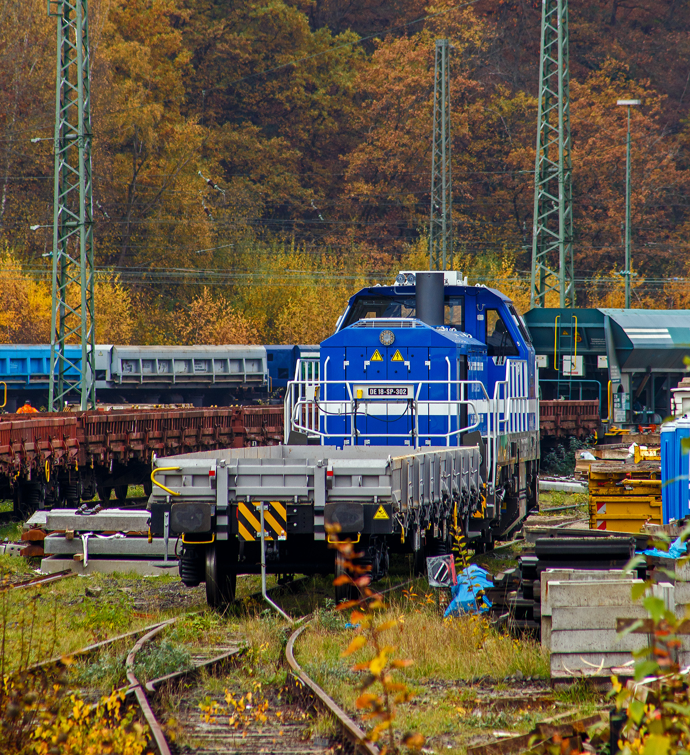 Die sehr neue SPITZKE DE18-SP-302 / 4185 302-1 (92 80 4185 302-1 D-SLG) eine dieselelektrische Vossloh DE 18 der SPITZKE SE steht am 08 November 2025 hinter einem Res-Wagen im Rbf Betzdorf/Sieg. 

Die DE18 wurde 2025 von der Vossloh Rolling Stock GmbH in Kiel unter der Fabriknummer 5502655 gebaut und am 14.08.2025 an die SPITZKE SE, Großbeeren ausgeliefert (Tag der Überführung).

Die Diesellokomotive der Baureihe DE 18 ist insbesondere für den schweren Rangier- und Streckenbetrieb mit hoher Zugkraft geeignet. Sie gilt als aktuell leistungsstärkste Mittelführerhauslokomotive auf dem europäischen Markt. Die DE 18 ist für den Rangierbetrieb mit einer Funkfernsteuerung ausgerüstet und ist für bis zu drei Loks mehrfachtraktionsfähig. Durch Energiesparmodus und Start-Stopp-System reduziert sie Schadstoffausstoß und spart Treibstoff ein, zudem besitzt sie einen Rußpartikelfilter. Zusätzlich lässt sich der Kraftstoffverbrauch durch ein effizientes Motormanagement und einer Begrenzung der Motorleistung, wenn nicht die Maximalleistung benötigt wird, reduzieren. Der 1.800 kW starke MTU Dieselmotor wird durch ein Batteriepaket ergänzt, das einen bis zu einstündigen emissionsfreien Rangierbetrieb gewährleistet und Fahrten durch Null-Emissions-Bereiche etwa in Tunneln, Werkhallen oder Bahnhöfen, ermöglicht.

Die Lok hat eine Anfahrzugkraft von 300 kN und eine Dauerzugkraft von 230 kN bei 24.2 km/h. Höchstgeschwindigkeit beträgt 120 km/h, die kleinste Dauerfahrgeschwindigkeit 3 km/h,
