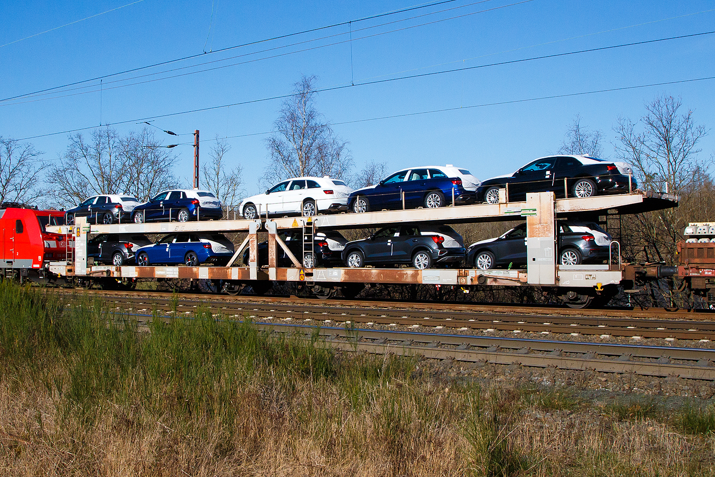 Doppelstock-Autotransportwagen 23 80 4351 950-9 D-ATG, der Gattung Laaes 556, der DB Cargo Logistics GmbH (ex DB Schenker ATG) am 07.02.2023 im Zugverband bei einer Zugdurchfahrt in Wilnsdorf-Rudersdorf.

Der Wagen wurde 1992 Waggonbau Niesky gebaut.

Die Waggons haben zwei Ladeebenen und können je nach Bauart mit 9 bis 14 Mittelklasse-Pkw beladen werden. Die Waggons sind europaweit einsatzfähig und wurden gezielt für den internationalen Transport von PKW entwickelt. Zur Be- und Entladung der oberen Ladeebene an Kopframpen können die Wagenenden aus der Transportstellung in die sogenannte Rampenstellung abgesenkt beziehungsweise angehoben werden. Des Weiteren können die Wagenenden der oberen Ladeebene in die Beladestellung angehoben werden. Hierdurch wird die maximale Durchfahrtshöhe für die Be- und Entladung der Fahrzeuge auf der unteren Ladeebene realisiert.

TECHNISCHE DATEN:
Gattung: Laaes (Bauart 556)
Spurweite: 1.435 mm
Anzahl der Achsen: 4
Länge über Puffer : 27.000 mm
Achsabstand: 22.300 mm (9.000 / 4.300 / 9.000 mm)
Laufraddurchmesser: 840 mm (neu)
Ladelänge : 26.100 mm (unten) / 26.500 mm (oben)
Höchstgeschwindigkeit: 100 km/h (120 km/h leer)
Eigengewicht: 28.800 kg
Nutzlast: 24 t ab Streckenklasse A, unten max. 13 t / oben max. 11 t
Kleinster befahrb. Gleisbogenhalbmesser: 80 m
Bremse: KE-GP-A (LL)
Intern. Verwendungsfähigkeit: RIV