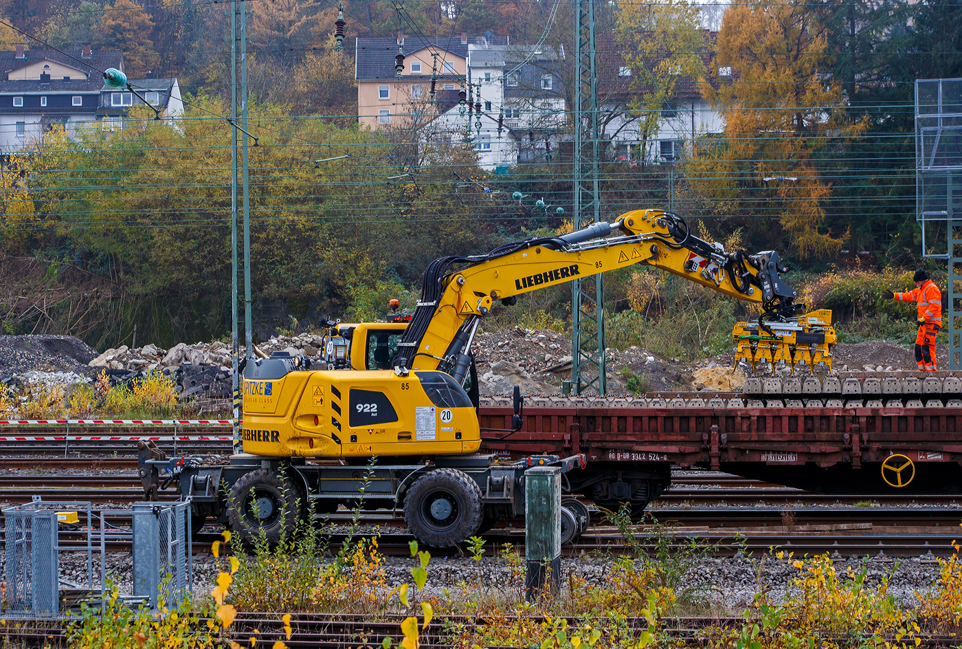 Ein LIEBHERR Zweiwegebagger A 922 Rail Litronic der SPITZKE SE (Großbeeren) mit angebautem Schwellenverlegegerät Typ 159-5 greift sich die nächsten 5 Schwellen von einem Res-Güterwagen und verlegt diese im neuen Gleisbett im Rbf Betzdorf/Sieg am 08. November 2025. Hier werden zurzeit Gleise erneuert.