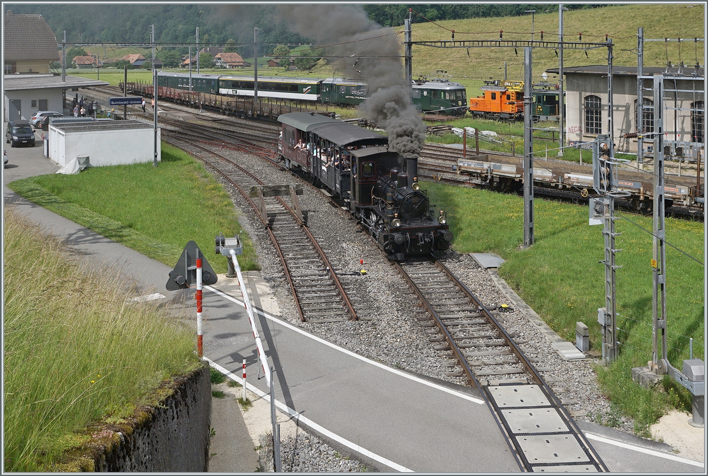 Mit einem Dampfzug der  Emmentalbahn  verlässt die E 3/3 853 (UIC 90 85 0008 573-3) den Bahnhof von Sumiswald-Grünen mit dem Ziel Wasen im Emmental. Im Hintergrund ist der VH-MThB ABe 4/4  N° 12 mit Bodan-Salon-Wagen und dem VH-MThB BDt zu sehen, der vor einer guten halben Stunde Sumiswald erreicht hat. 
Zudem wird in Kürze der OeBB Dampfzug aus Balsthal in Sumiswald eintreffen. 
Kurz zusammengefasst: heute findet der Gotthelf-Märit in Sumiswald statt. 

14. Juni 2025