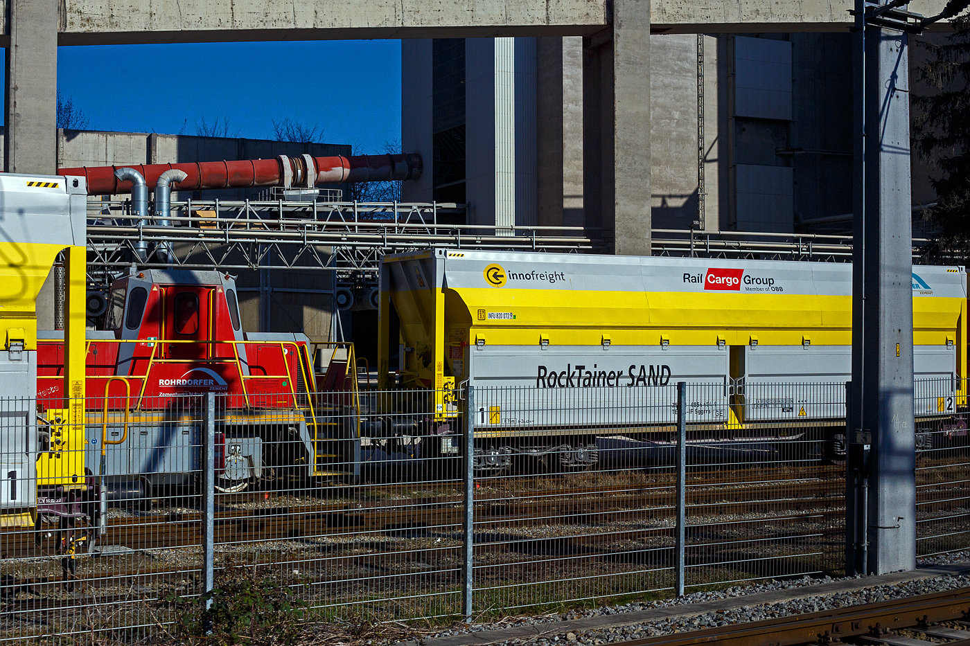 Noch schnell aus dem Zug, daher leider nur ein Ausschnitt erwischt. Der Vollert
Rangier-Robot DER 120 Pro Eco | Shunting Robot DER 120  Henriette  der Rohrdorfer Zement GmbH / Zementwerk Hatschek GmbH, rangiert am 03 April 2025 in Gmunden einen RockTainer SAND-Zug am Werksgelände zur Anschlussstelle. 

Der Robot DER 120 ist ein zweiachsige Rangierlok mit diesel-elektrischem Antrieb vom Hersteller Vollert Anlagenbau GmbH in Weinsberg (Deutschland). Der elektrische Antrieb hat nicht nur einen hervorragenden Wirkungsgrad, sondern garantiert auch ein konstant hohes Drehmoment. Die Leistung ist somit umgehend bei niedrigen Motordrehzahlen abrufbar und verschafft dem Rangier-Robot ein völlig neues Fahrgefühl mit unglaublicher Schubkraft vom Stand weg. 

Der wassergekühlte 6-Zylinder-Reihenmotor mit Turboaufladung, Ladeluftkühlung und externer Abgasrückführung hat eine Leistung von 180 kW (245 PS), so verhilft er dem Robot DER 120 über eine Zugkraft von 120 kN. Der powerMELA-Generator ist über ein Verteilergetriebe an den Dieselmotor angebunden. Dieser wandelt die vom Diesel erzeugte mechanische Energie in elektrische um und versorgt damit die Antriebsmotoren. Diese sind mit einem Stirnradgetriebe kombiniert und treiben die Achsen an.
