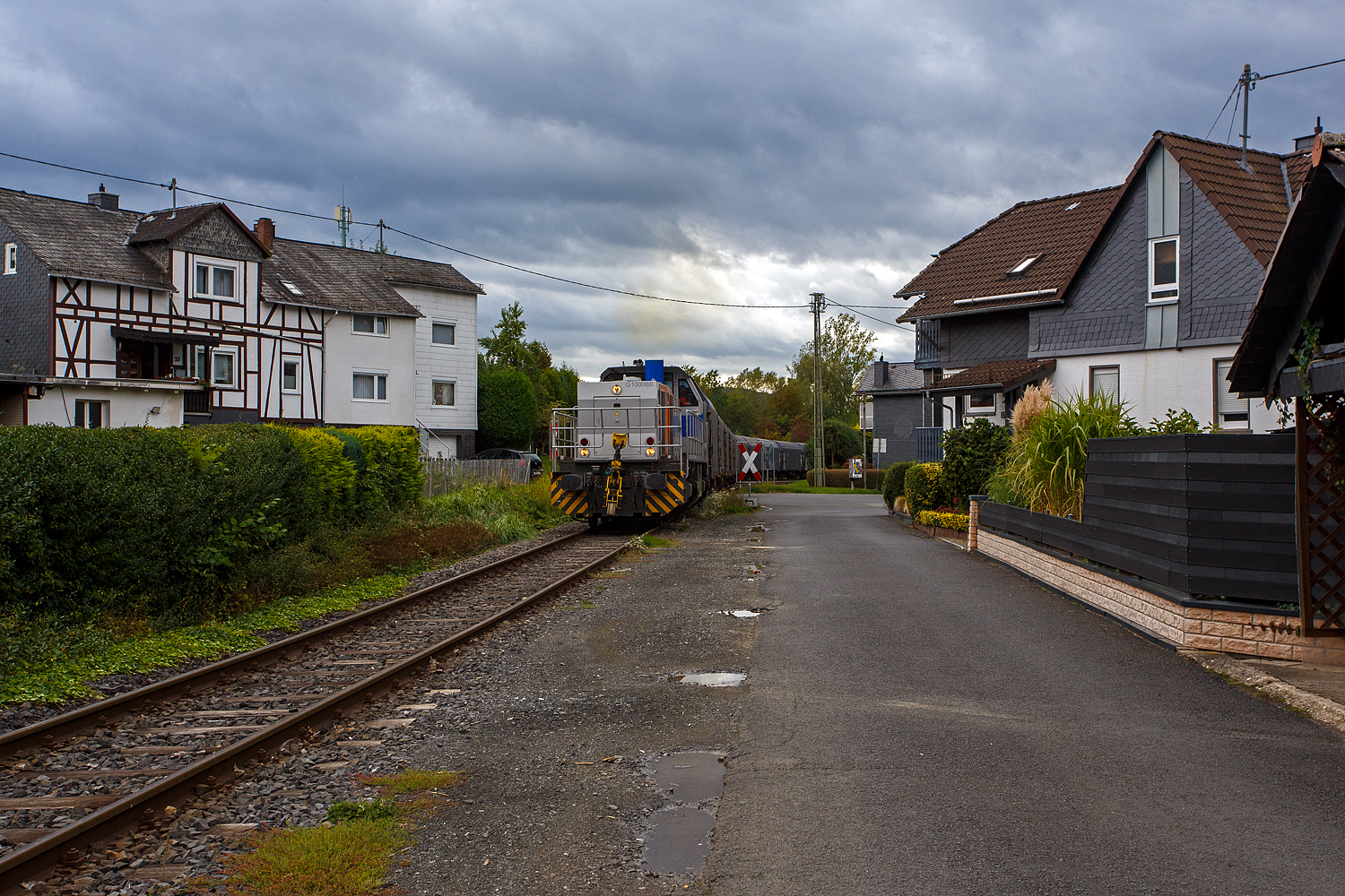 Nun hat die KSW 47 (92 80 1271 027-5 D-KSW), ex D 2 der HFM, eine Vossloh G 1000 BB der KSW (Kreisbahn Siegen-Wittgenstein), den Coilzug übernommen und zieht diesen nun vom KSW Rbf Herdorf weiter zu den Schäfer Werke KG am Pfannenberg in Neunkirchen-Salchendorf. Hier geht es gerade in Neunkirchen-Struthütten am 18 September 2025 zwischen den Häuser und Hecken hindurch. 

Auch wenn hierdurch, mehrmals täglich, die Anwohner genervt werden, zu Einem durch die Rollgeräusche und vor allem durch das erforderliche Pfeifen (Hupen) der Loks, wegen der vielen Bahnübergänge. Aber dennoch ist es schon lange praktifizierter Umweltschutz, denn mit allein dieser Zug ersetzt 40 bis 50 LKW. Übrigens diese Bahnstrecke der ehemaligen Freien Grunder Eisenbahn AG (auch bekannt als „Talbahn“) gibt es seit 1904, heute gehört sie als Betriebsstätte FGE -Freien Grunder Eisenbahn zur KSW Kreisbahn Siegen-Wittgenstein GmbH und wird als Freien Grunder Eisenbahn NE 447 (DB - Streckennummer 9275) geführt.

Mit einer eigenen Schieneninfrastruktur im Kreis Siegen-Wittgenstein, die mehr als 30 Kilometer umfasst, verfügt die KSW über wichtige Kapazitäten im wachsenden Güterverkehr. Auch wenn in Deutschland der Schienen-Güterverkehr geringer geworden ist, so ist er hier auf der „Talbahn“ die letzten Jahre ungemein gewachsen. 

Früher gab es ich Siegen (Eintracht) noch einen Abschnitt, wo die KSW bzw. frühere Siegener Kreisbahn auf der Eiserfelder Straße mit Läute (Glocke) fuhr, so wurde diese Bahn auch gerne im Volksmund „Bimmelbahn“ genannt.