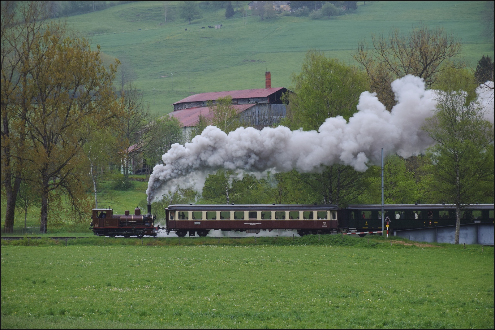 Vapeur Val-de-Travers: Train  Au fil de l'Areuse .

E 3/3 8511 nimmt mit Getöse schon beim ehemaligen Asphaltwerk in La Presta Anlauf für die Steigung nach Travers. Mai 2023.