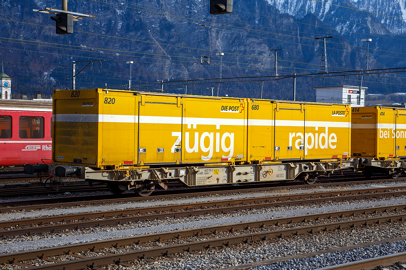 Zweiachsiger Behältertragwagen 43 68 4433 192-2 D-AAEC, der Gattung Lgnss 1 der ehemaligen AAE Ahaus-Alstätter Eisenbahn Cargo AG mit Sitz in Baar (2015 zur VTG AG, Hamburg) vermietet an die Schweizerische Post AG, beladen mit zwei Wechselbrücke (WB) am 20 Februar 2017 abgestellt im Bahnhof Landquart.

Die Schweizerische Post AG (ex PTT) betreibt für den schweizweiten Brief- und Paketversand, aber auch Stückgutlogistik von palettisierte Handelswaren, Rohstoffen oder Gefahrgut andere Kunden, einen Kombiverkehr von Tür zu Tür. Die Post verlädt die Waren von der Straße auf die Schiene und liefert sie an die gewünschte Adresse in Post eigenen oder Kunden Wechselbehälter oder Containern. Für die Wechselbehälter oder Container gibt es Umschlagsterminals der Post in Daillens, Härkingen, Frauenfeld, Landquart oder Cadenazzo.

Um den schweizweiten Brief- und Paketversand schneller und letztlich auch wirtschaftlicher zu gestalten, investierte die Schweizer Post massiv in den Aufbau einer Logistik, die den Wechselbehälter als tragendes Element vorsieht. Um auch die Eisenbahn in dieses System einzubeziehen und nicht, wie in vielen anderen Ländern geschehen, nahezu ausschließlich auf die Straße als Verkehrsträger zu setzen, musste ein geeigneter Tragwagen gefunden werden.
Die Rollmaterialknappheit im Kombinierten Verkehr ist jedoch so alt wie der KV selbst. Zudem hatte es Ende der 1990er Jahre kaum für das Anforderungsprofil geeignete Waggons. Immerhin sollten je Waggon zwei Behälter (WB) transportiert werden können. Vierachsige Waggons waren hierzu eindeutig 
überdimensioniert und wären durch viel ungenutzte Ladelänge sowie großer »Totlast« unwirtschaftlich gewesen. Die meisten Vierachser sind ausgelegt für 60' Ladelänge und somit gut geeignet für ISO-Container,  nicht jedoch für die Wechselbrücken, deren Längenmaße zwischen 23,5' (7,15m) und knapp 26' (7,82m) liegen.

Zweiachsige Waggons wurden jedoch wseit den 1980er Jahren europaweit kaum noch neu gebaut, da sie für den Containertransport aufgrund der maximalen Achslast nur begrenzt nutzbar sind. Zudem sorgten auch unerfreuliche Vorfälle von Entgleisungen im Rangierbetrieb solcher Waggons mit langem Achsstand für eine Abkehr vom Zweiachser. Während die UIC maximal 9 m vorsieht, lassen sich Ladelängen für Wechselbehälter oft nur mit 10 m Achsstand realisieren. Damit war klar, dass für den geplanten Einsatz nur eine Neukonstruktion in Frage kam.

So beauftragte die Schweizer Post die Ahaus-Alstätter-Eisenbahn (AAE) in Baar, damals einer der größten Waggonvermieter Europas (gehört seit 2015 zur VTG AG) mit Konstruktion und Lieferung eines geeigneten Waggons, der dann langfristig von der Post angemietet werden sollte. Die AAE ließ daraufhin bei MSV Studenka (Tschechische Republik) einen zweiachsigen Behältertragwagen bauen, der mit einem Radstand von 10 m eine Ladelänge von 15 m aufweist und somit geeignet für das geforderte Beladungsszenario von zwei 7,45m Wechselbehältern (C745) ist.

Der Wagenrahmen besteht aus einer geschweißten Stahlkonstruktion mit außenliegenden fischbauchartigen Längsträgern in Doppel-T-Profil. Weiterer wichtiger Aspekt war, die Konstruktion nicht nur lauf-, sondern auch bremstechnisch für ss-Verkehre (HG 120 Km/h) auszulegen. Lauftechnisch wird dieses erreicht durch Einsatz von zwei längseingebauten Wende- sowie vier Querdämpfern zwischen Radsatzlagern und Wagenrahmen. Bremsseitig verfügt der Waggon über eine selbsttätig lastabhängig wirkende Druckluftbremse. Die Bremskraft wird dabei über jeweils zwei Aluminiumkeramik-Bremsscheiben pro Achse übertragen. Die Anbringung der Bremszangen an zwei massiven, querliegenden Rohrkonstruktionen verleiht dem »Postwagen«, zusammen mit Dämpfern und Fischbauchträgern, sein charakteristisches Aussehen.

Die Ladeflächenhöhe liegt durchgehend bei 1.070 mm über SO und unterschreitet somit die gemäß UIC-Merkblatt 571-4 (Einheitsgüterwagen – Güterwagen des kombinierten Verkehrs) vorgesehene Normalhöhe um 100 mm. Bei einem Eigengewicht von 14 t weist der »Postwagen« eine für den Einsatzzweck in der Brief- und Paketlogistik geeignete Lastgrenze von 26 t (ss-Verkehre) resp. 31t (s) auf. Das Maximalgewicht des Wagens liegt somit bei 45 t, im Betrieb werden 31,6 t als Normgewicht angesetzt (die Ladeinheiten werden im Post-Betrieb nicht verwogen!).

Trotz zusätzlich an den Wagenenden eingebauter Schwingungsdämpfer, die Schwingungen der Waggonstruktur bei teilbeladenen Waggons verhindern sollen, verkehren die »Postwagen« entweder leer oder immer mit zwei Behältern beladen, selbst wenn einer davon leer mitgeführt wird.

Inklusive drei Prototypen wurden 1999 in gesamt 253 Wagen gebaut und bei der AAE in Dienst gestellt. Alle Einheiten sind in RAL 7044 seidengrau lackiert. Als zweiachsiger Tragwagen trägt der »Postwagen« die Bauartbezeichnung Lgnss und ist gemäß UIC 438-2 (Kennzeichnungen der Güterwagen) eingereiht als (43 68) 4433 000 – 252. Die Kennzeichnung 43 verweist dabei auf die nicht vorhandene RIV-Kompatibilität, da der Wagen nur innerhalb der Schweiz eingesetzt wird, aber eingestellt sin sie in Deutschland.

TECHNISCHE DATEN:
Gattung: Lgnss 1
Spurweite: 1.435 mm (Normalspur)
Anzahl der Achsen: 2
Länge über Puffer : 17.300 mm
Achsabstand: 10.000 mm
Ladelänge : 15.000 mm (zwei Wechselbehälter [C745] 7,45 m lang)
Ladehöhe über SOK: 1.070  mm 
Max. Zuladung bei Lastgrenze S: 31,0 t (ab Streckenklasse D)
Max. Zuladung bei Lastgrenze SS: 26,0 t (ab Streckenklasse C)
Max. Geschwindigkeit: 100 km/h (Lastgrenze S) / 120 km/h (bei Lastgrenze SS oder leer)
Eigengewicht: 13.600 kg
Bremse: DK-GP-A (D)
Handbremse: Ja
Verwendungsfähigkeit: Nur Schweiz

Quelle: kombimodell.waggonfabrik.eu, Schweizerische Post AG und eigene Sichtung der Anschriften 
