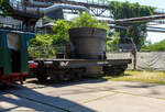 Ein vierachsiger normalspuriger offener Roheisenpfannenwagen der Burbacher Htte hinter der Normalspur-Dampflokomotive 46, einer Jung Hochofenlok niedriger Bauart, der Vlklinger Htte (ehem. Rchling'schen Eisen- und Stahlwerke GmbH in Vlklingen/Saar, ab 1982 ARBED-Saarstahl GmbH, ab 1986 Saarstahl Vlklingen GmbH), ausgestellt als Denkmal am Gelnde Vlklinger Htte, hier am 01 Juli 2025 am Gelnde Vlklinger Htte als Denkmal. Heutiger Eigentmer ist die Initiative Vlklinger Htte e.V..

1971 fusionierten die Burbacher und Vlklinger Htte, und ab 1975 wurde die Stahlproduktion in der Burbacher Htte eingestellt. Das Bild zeigt einen offenen Pfannenwagen, mit dem das flssige und heie Roheisen aus dem Hochofen aufgefangen wird, und dann zur Weiterverarbeitung mittels Werkseisenbahn zur Weiterverarbeitung in das angrenzende Stahl- und Walzwerk weitertransportiert wurde. Da die Entfernungen gering waren, bentigte man keine mit Schamott ausgemauerten Torpedopfannenwagen. Ob der Wagen hier auf der Vlklinger Htte ist mit nicht klar, aber da er erheblich hher ist als die Lok, so vermute ich das er hier keinen Einsatz fand.