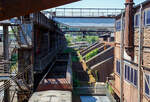 Am Tiefbunker (Rohstoffentladebunker der Sinterhalle) der Völklinger Hütte (ehem. Röchling'schen Eisen- und Stahlwerke GmbH in Völklingen/Saar, ab 1982 ARBED-Saarstahl GmbH, ab 1986 Saarstahl Völklingen GmbH) hinter der Normalspur-Denkmallok 34 stehen zwei vierachsige offene Schüttgutwagen (Sattelwagen) mit schlagartiger Schwerkraftentladung, hydraulischem Klappenverschlusssystem vermutlich der Gattung Falns (genaue Bezeichnungen kann man nicht erkennen), hier am 01 Juli 2025. Die Darstellung steht für den Rohstofftransport der Hütte zur Herstellung des Sintergutes. Die Lok war auch auf Bundesbahn Gleisen zugelassen. Heutiger Eigentümer der Lok und Wagen ist die Initiative Völklinger Hütte e.V..